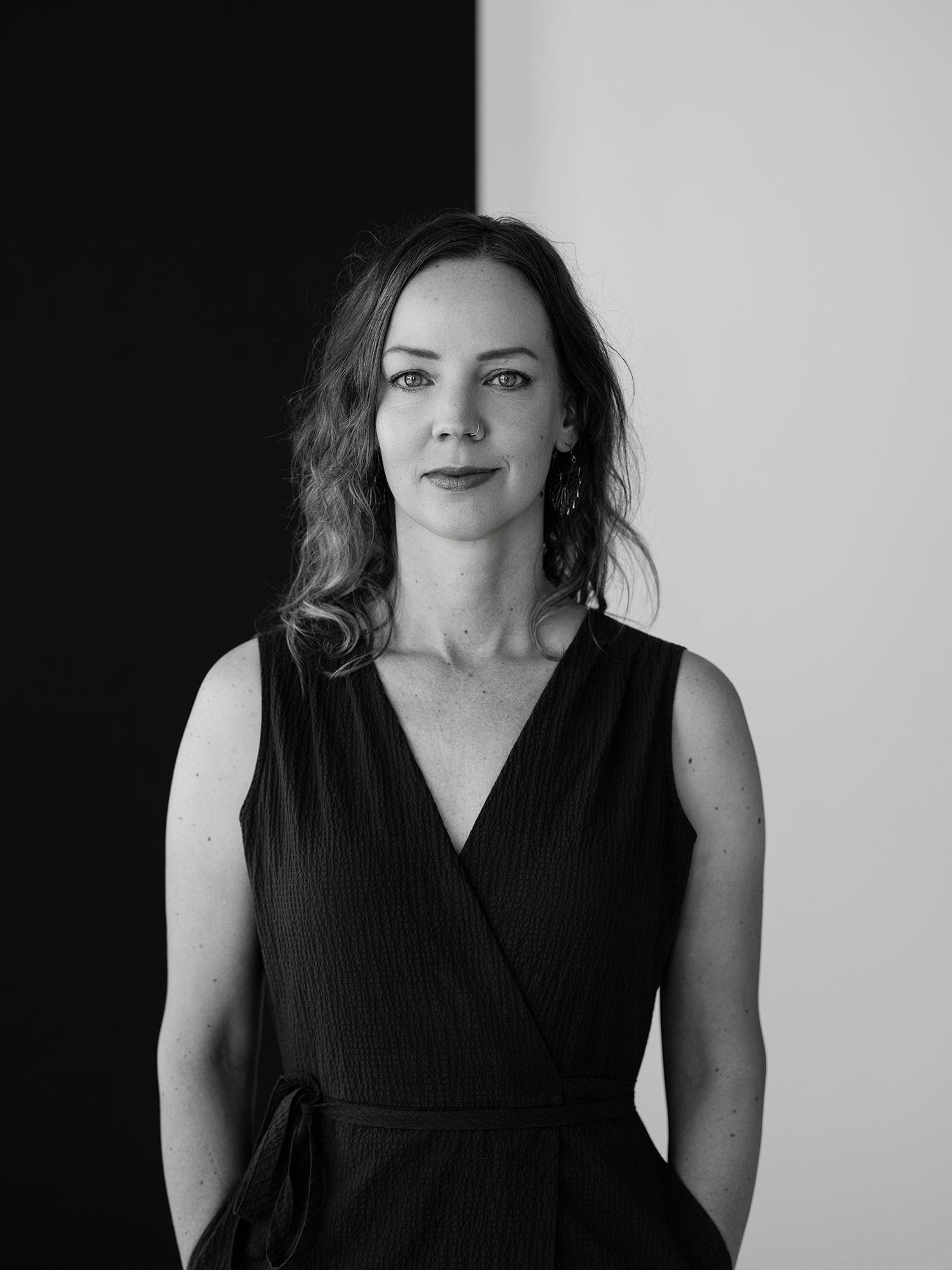 Debby Andersen, black-and-white portrait in a sleeveless wrap dress against a split black-and-white wall