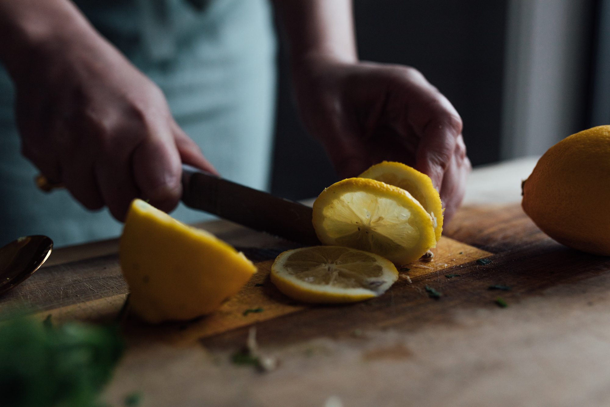 Hands slicing lemons on a wooden cutting board