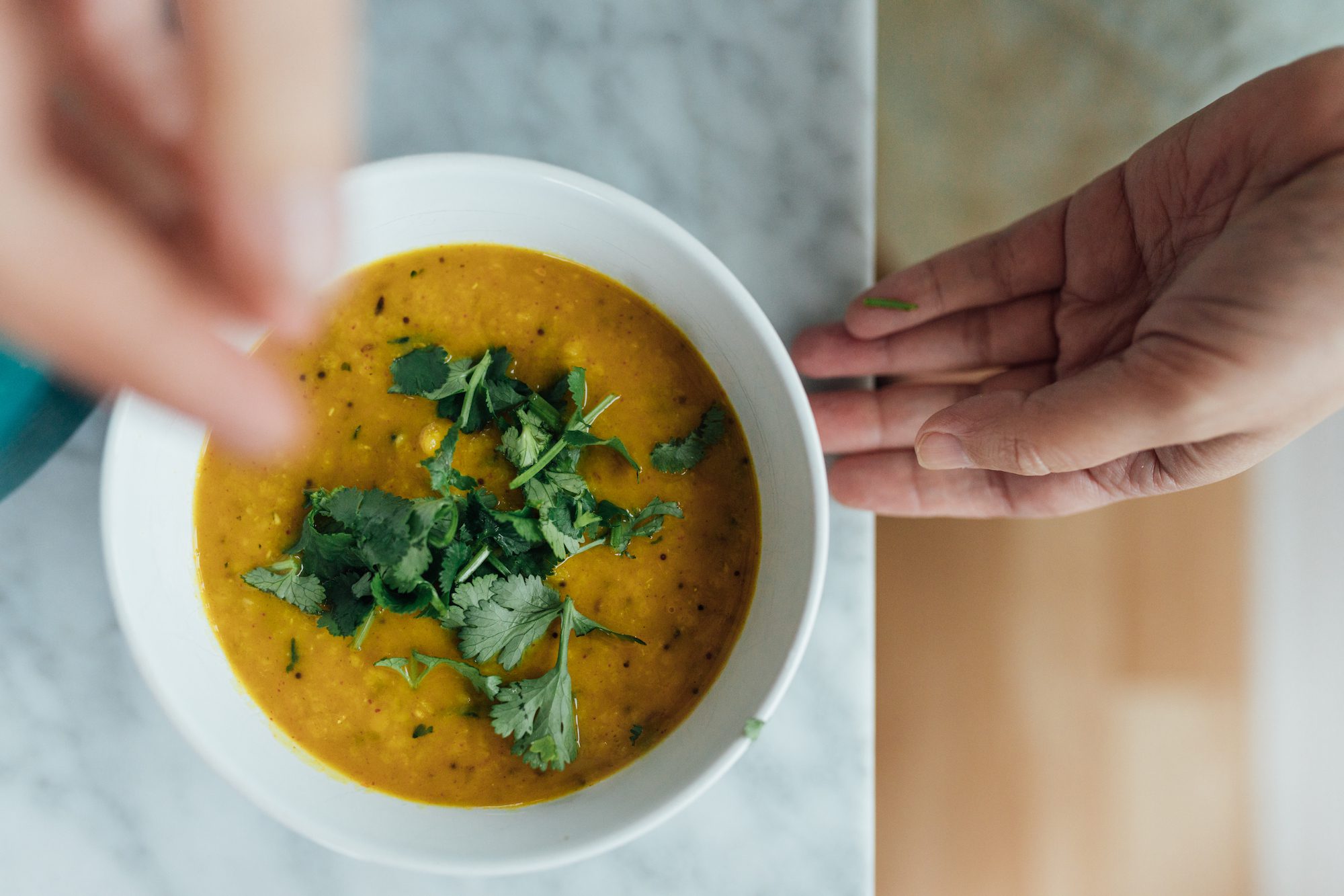 Overhead bowl of red lentil soup garnished with cilantro on a marble surface