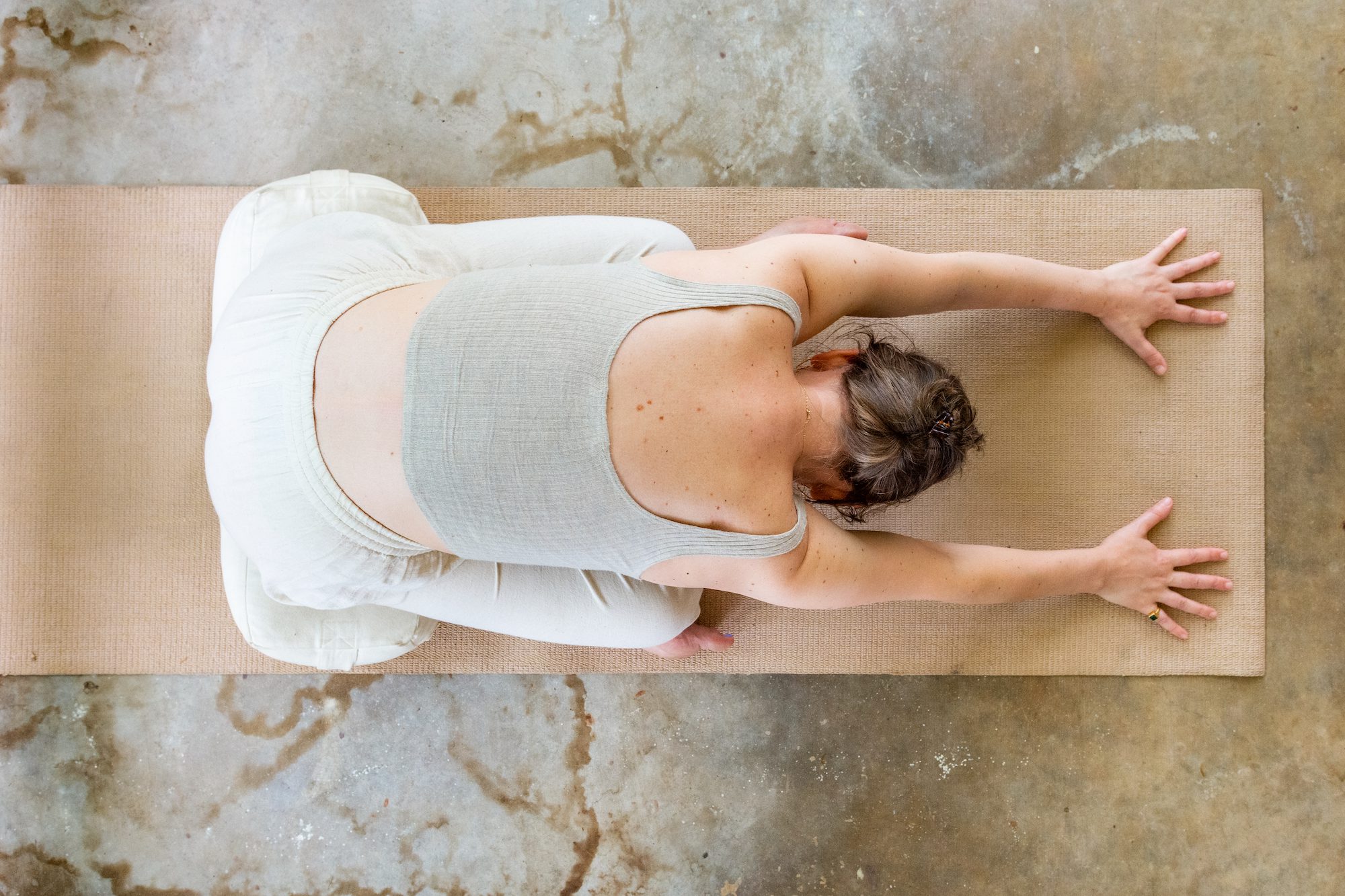 Aerial view of a woman in child's pose on a yoga mat on a concrete floor