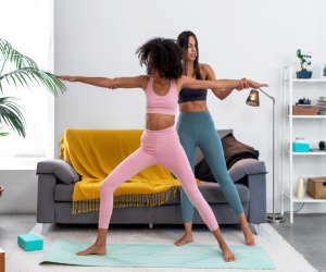 Two women practising a warrior pose together in a living room