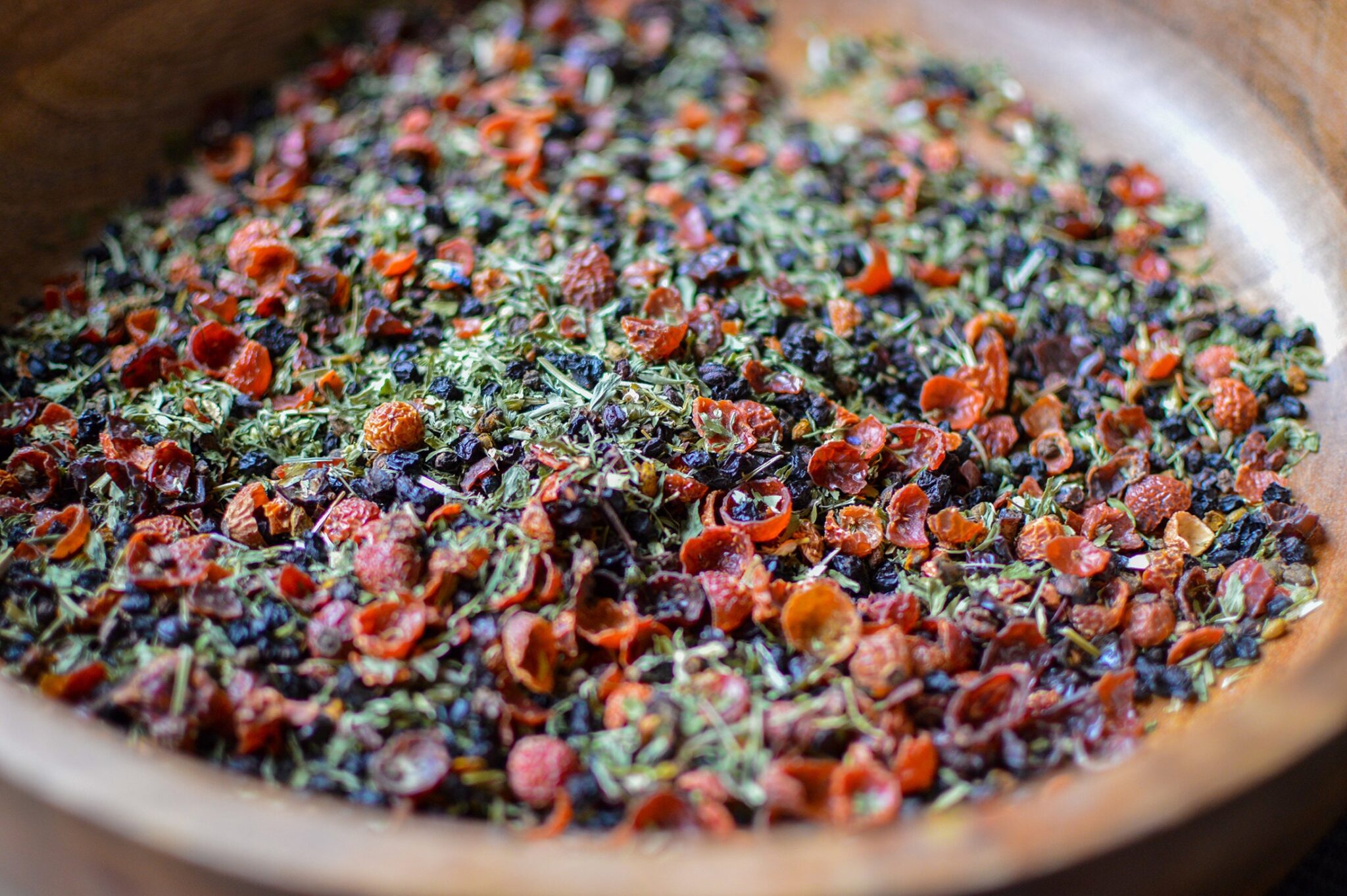 Close-up of a loose dried herbal tea blend with berries in a wooden bowl