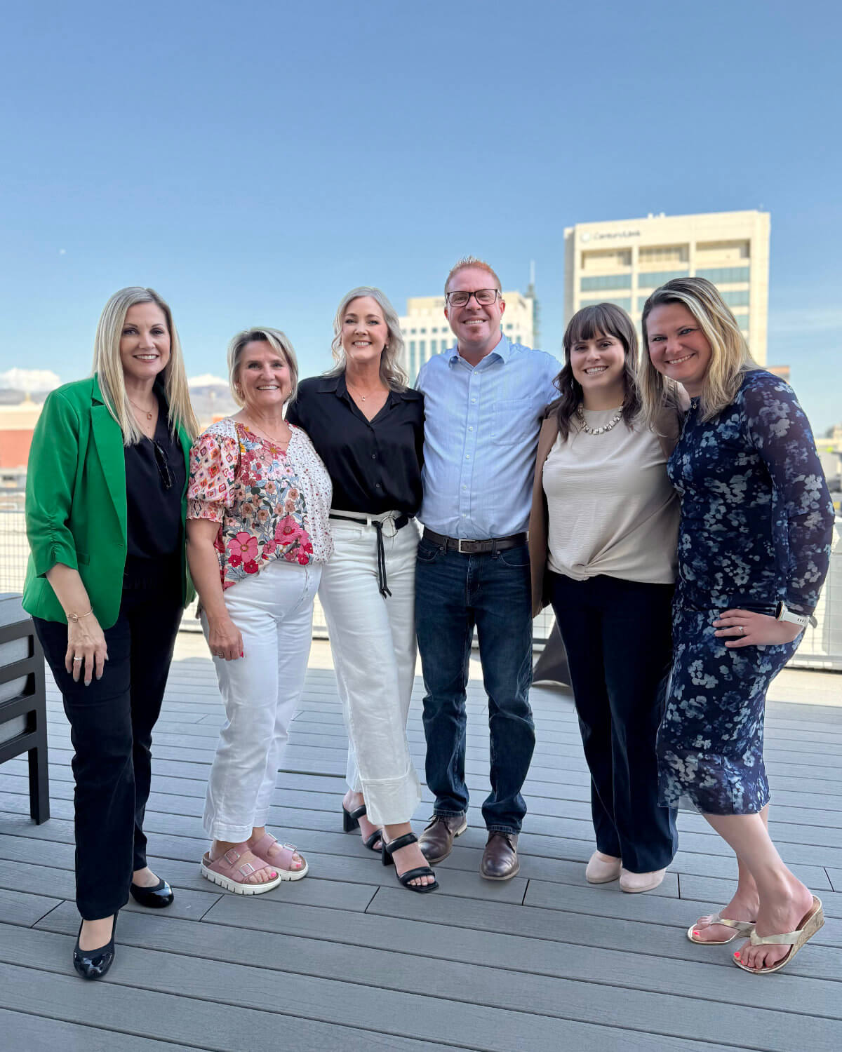 Allison Dunn with six clients on a rooftop deck, Boise skyline behind them