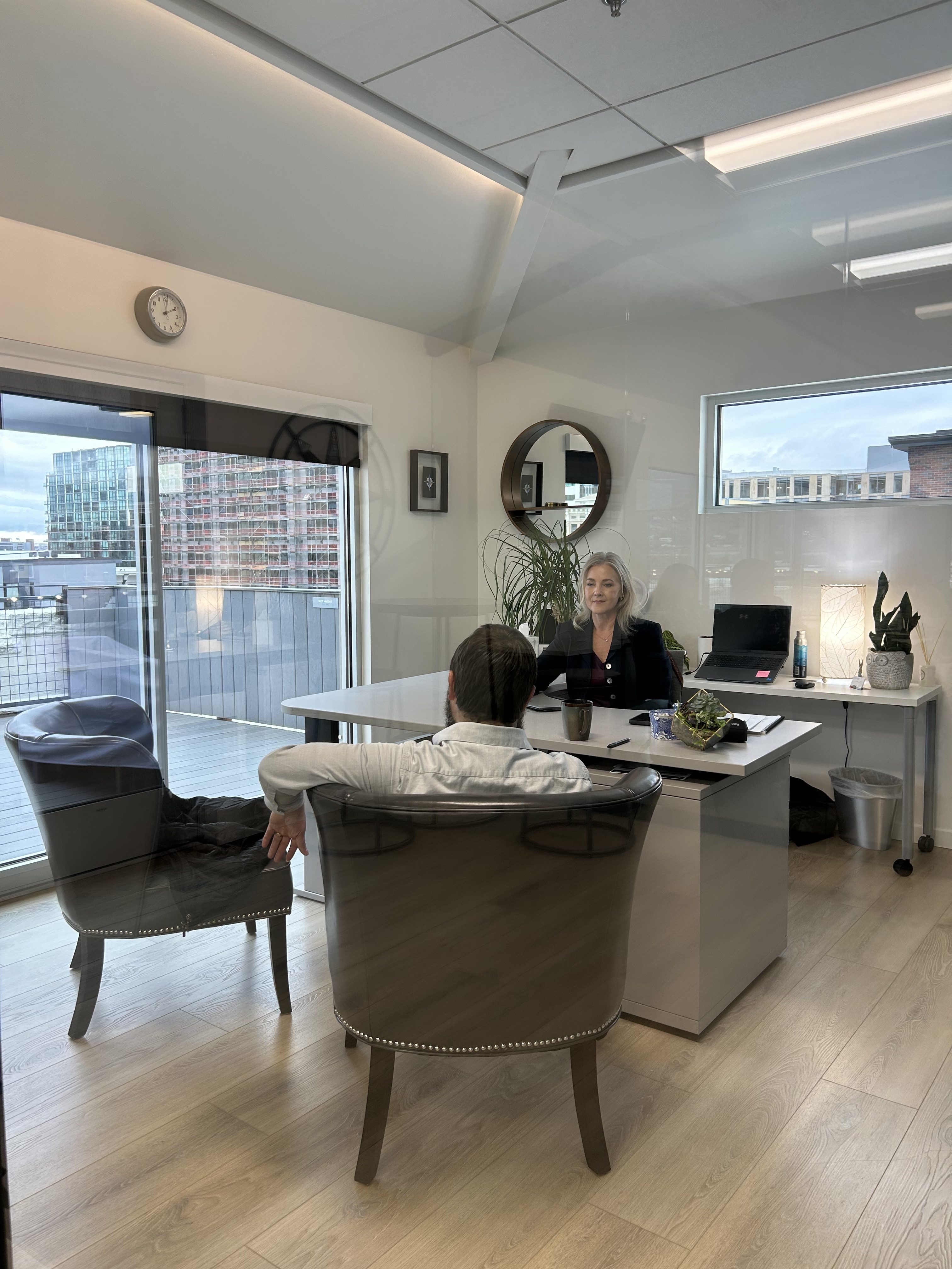 Allison Dunn seated at her desk in a modern office meeting with a client, city visible through the windows