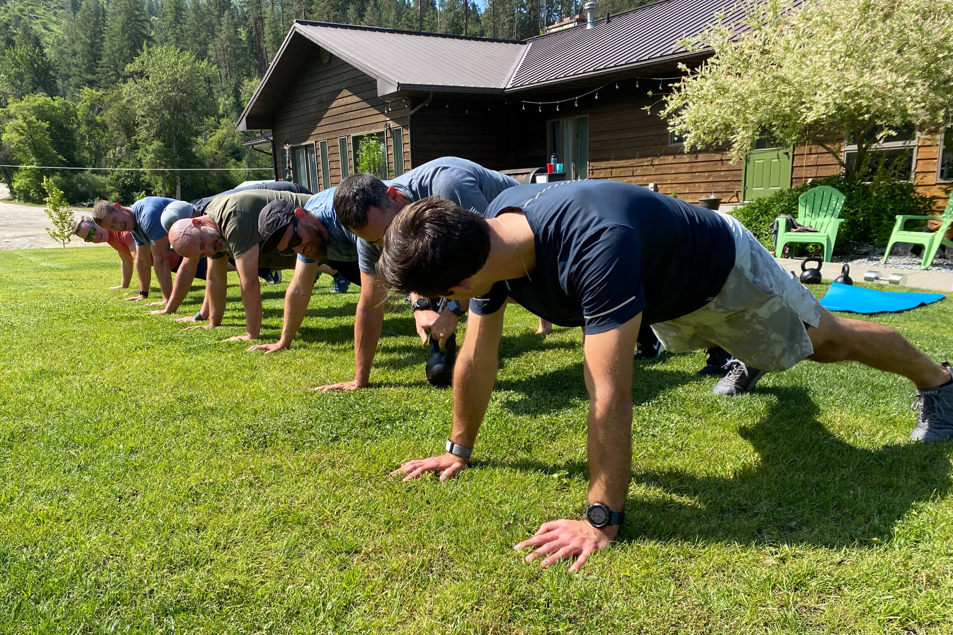 A group doing push-ups on a lawn outside a rustic cabin