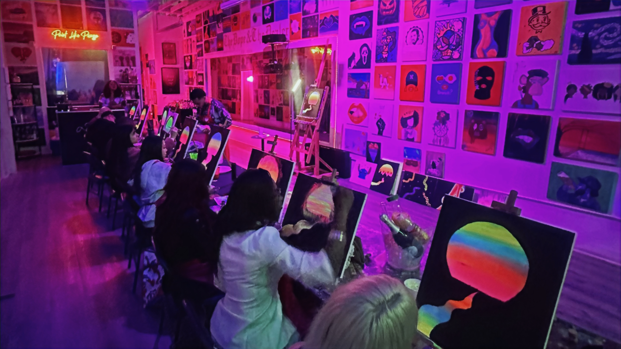 Group of people painting on canvases in a neon-lit paint and sip studio at Demi Lauren Studios