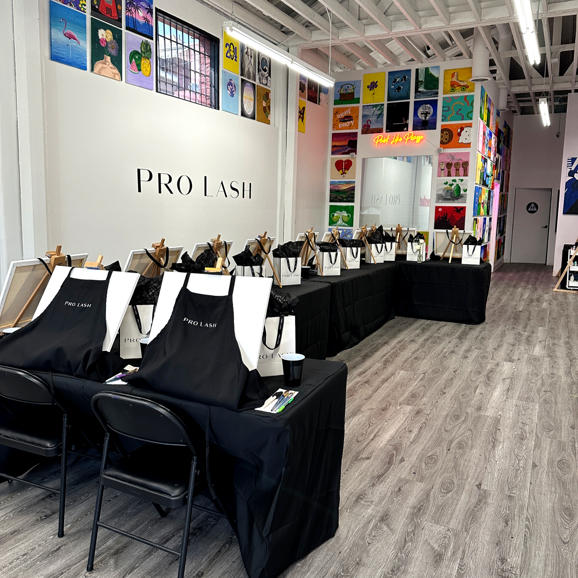 Studio set up for a private Pro Lash paint party with branded aprons and gift bags on black tables