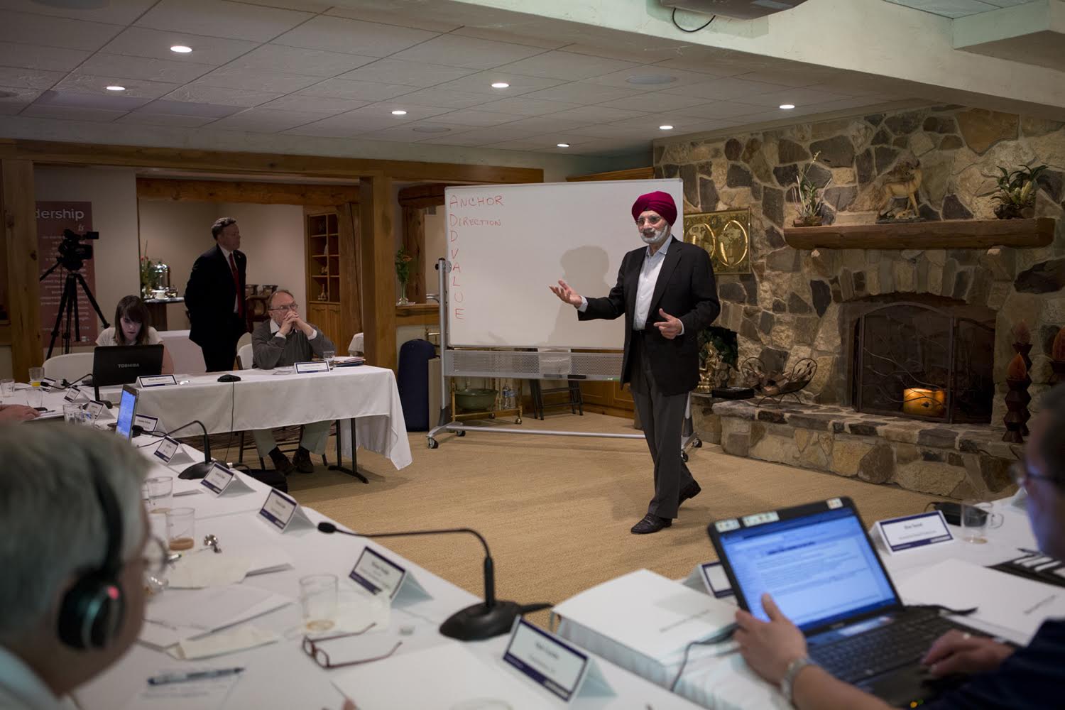 Ratanjit S. Sondhe leading a leadership workshop in a rustic lodge room with a stone fireplace and whiteboard