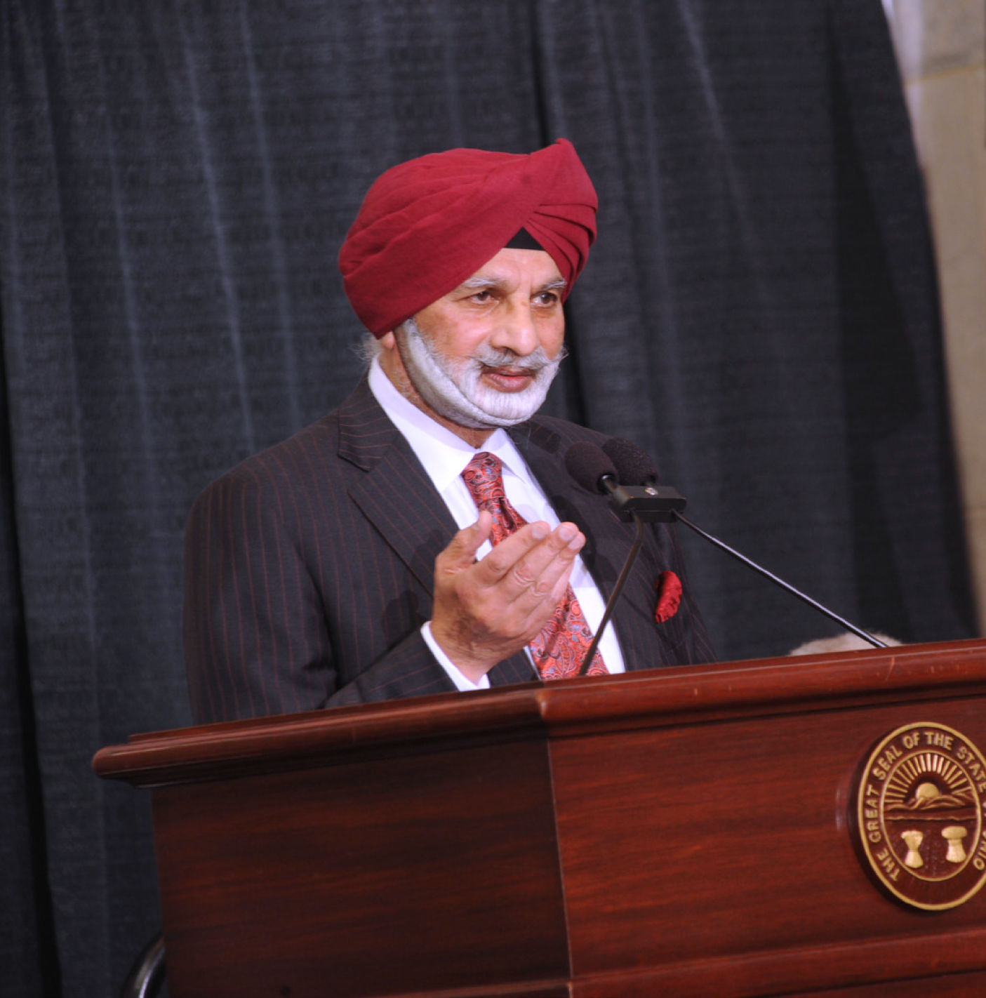 Ratanjit S. Sondhe in a red turban and dark pinstripe suit speaking at an official Ohio state podium