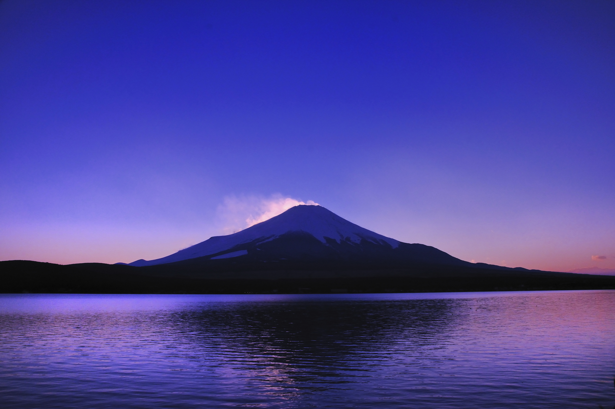 Snow-capped volcanic mountain at twilight reflected in a still lake beneath a deep blue-purple sky