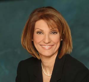 Portrait of Dr. Candace V. Love, smiling in a dark blazer and pearl necklace against a teal background
