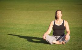 Woman sitting cross-legged meditating on a grass field outdoors