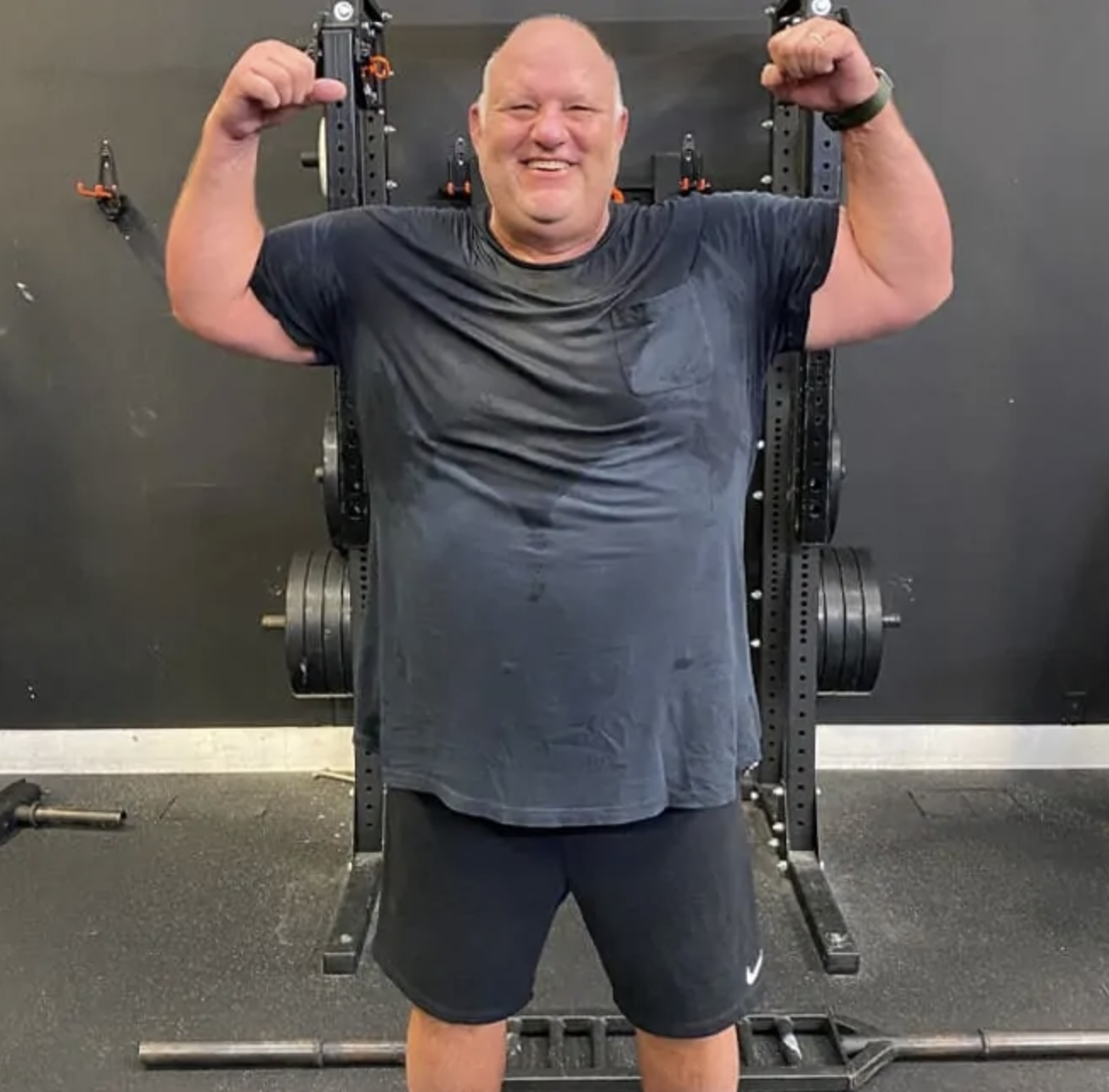 Gordon Johnson flexing with arms raised in front of a squat rack