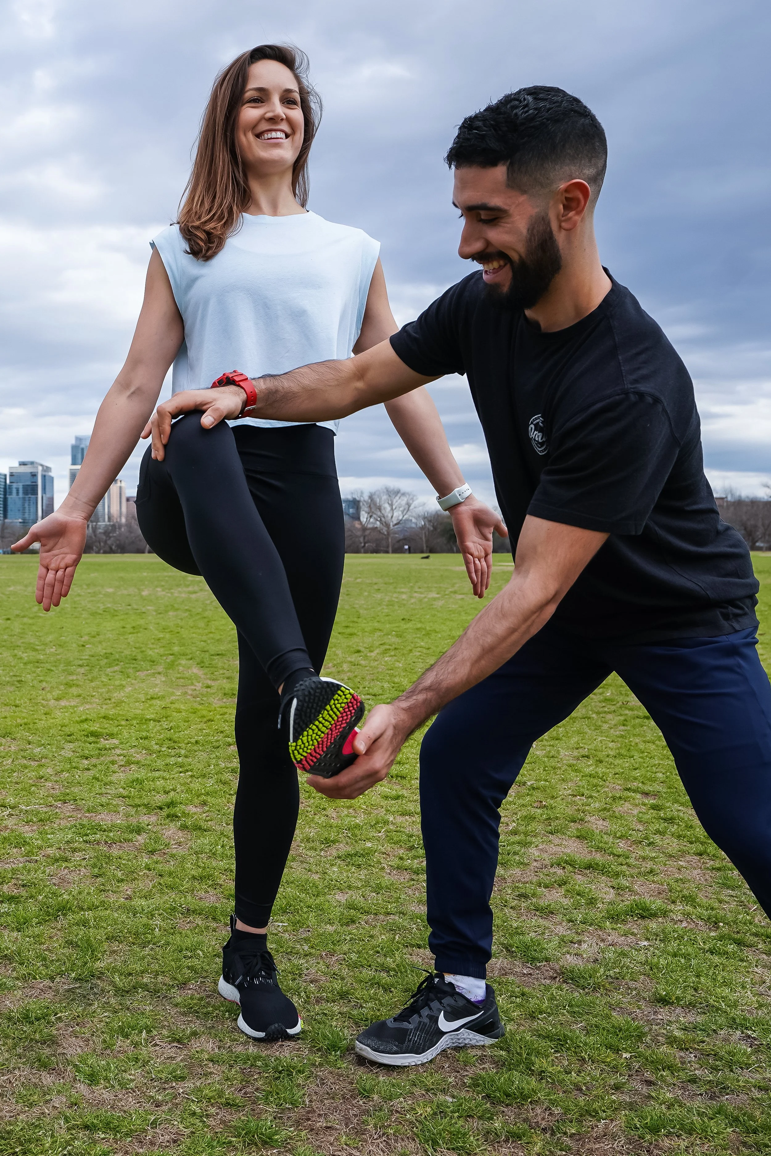 Cristian and Natalie, founders of Durable Athlete, doing a balance and mobility drill together in an Austin park with the skyline behind them