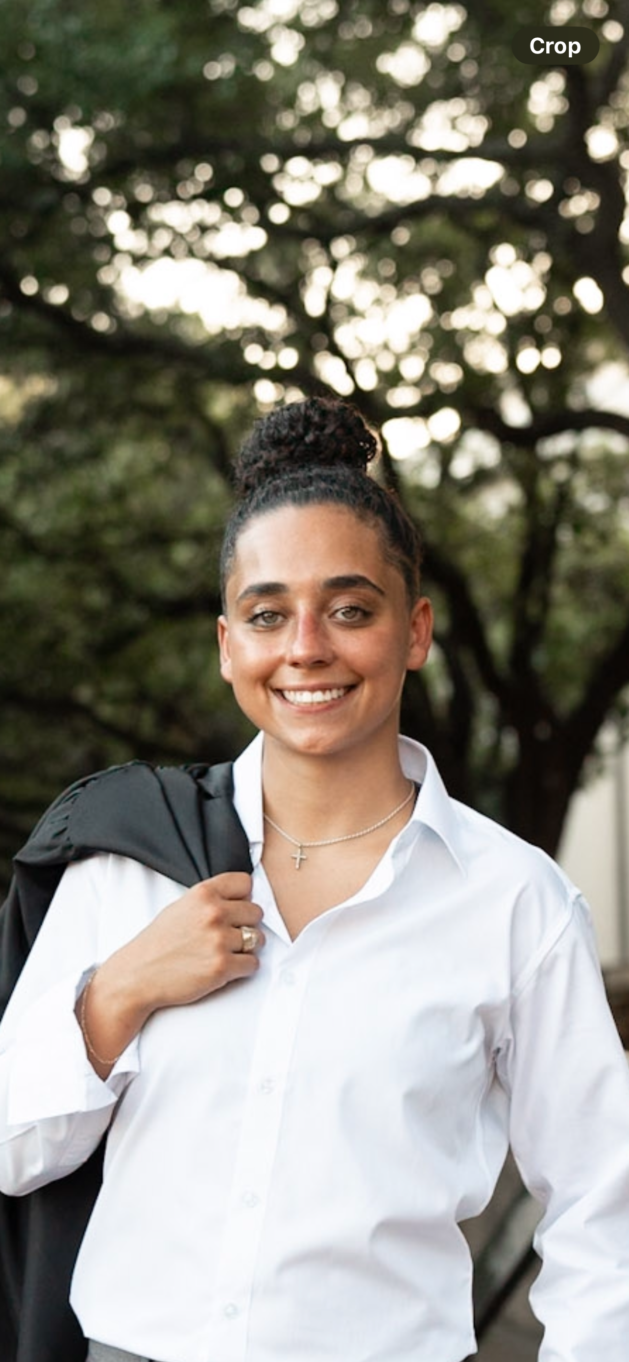 Layla Habash smiling outdoors in a white shirt with a graduation robe over her shoulder