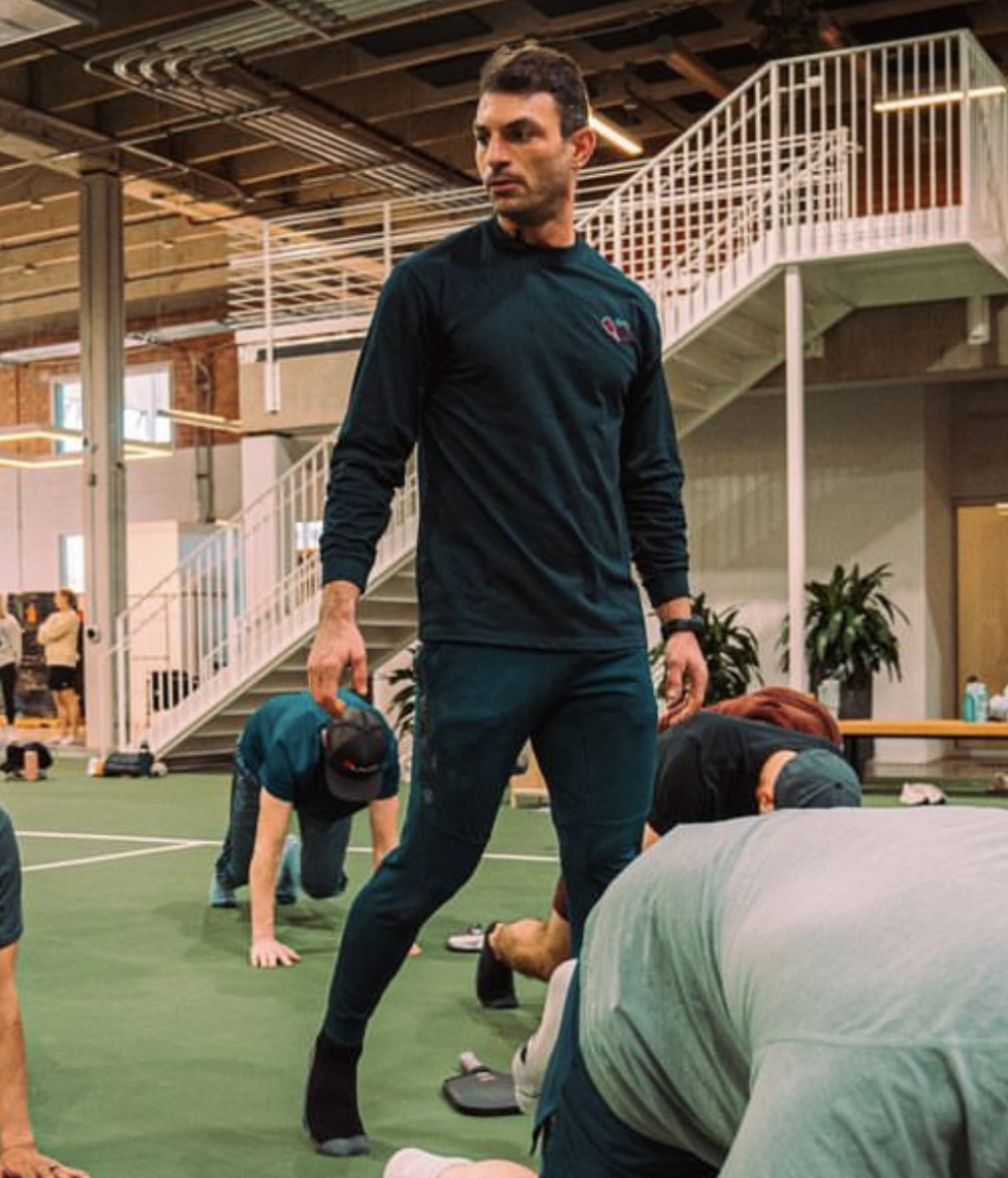 Joshua Orenstein overseeing a group doing floor work in an indoor turf facility