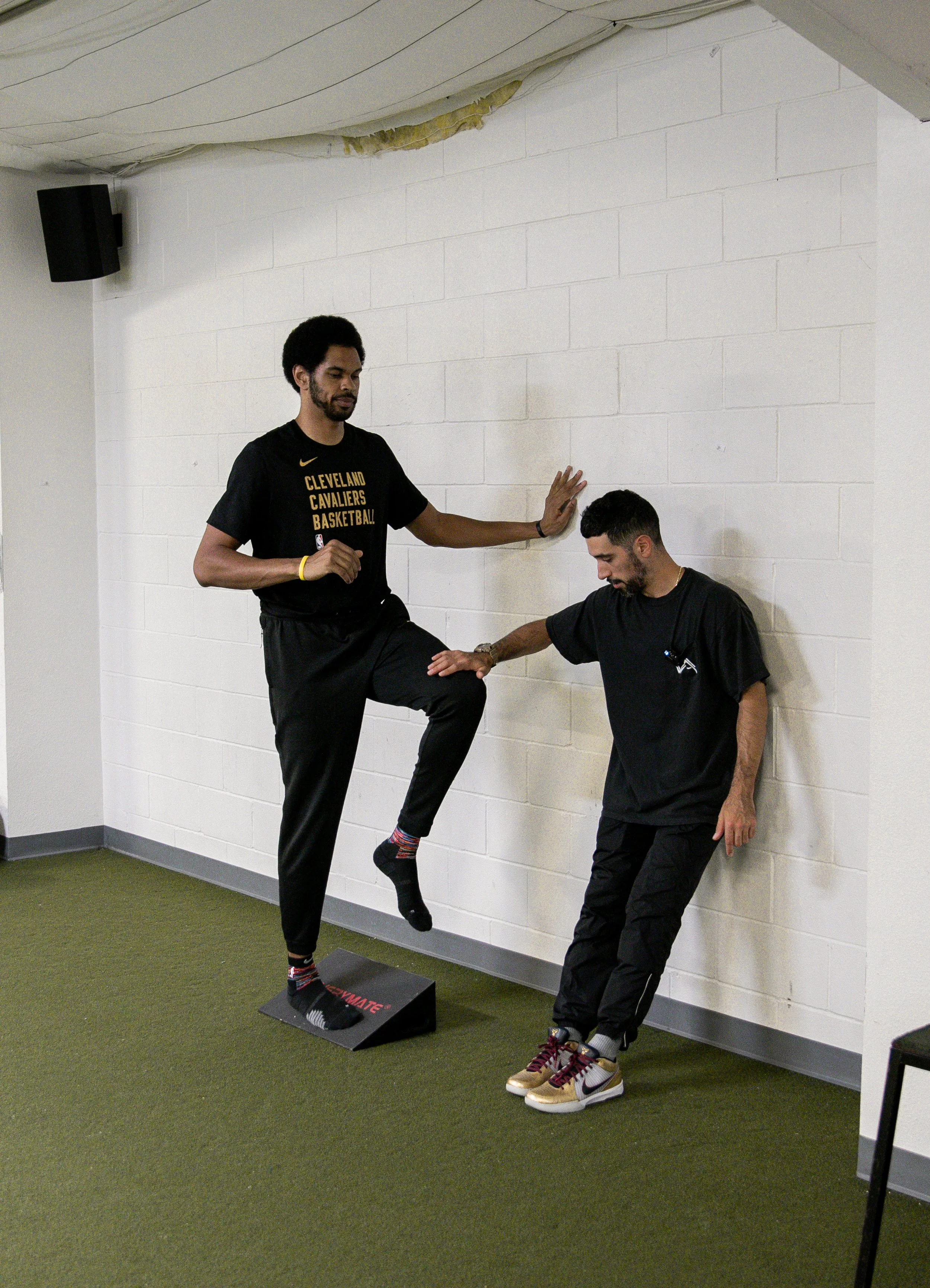 Jarrett Allen balancing on one leg on a ramp block in a Cavaliers shirt while the trainer guides him