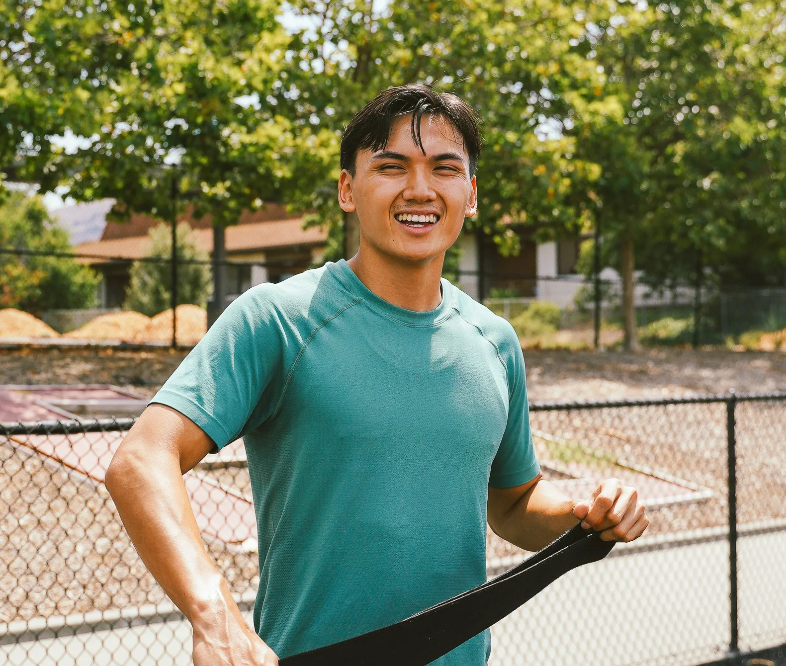 Dawson Dinh smiling in a teal shirt holding a resistance band outdoors near a court