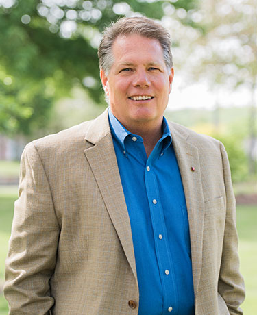 Mark Pierce, smiling, in a tan blazer and blue shirt outdoors