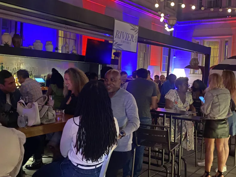 Crowd socializing at a bar under blue and red stage lighting at an Early Burdz museum mixer after-party