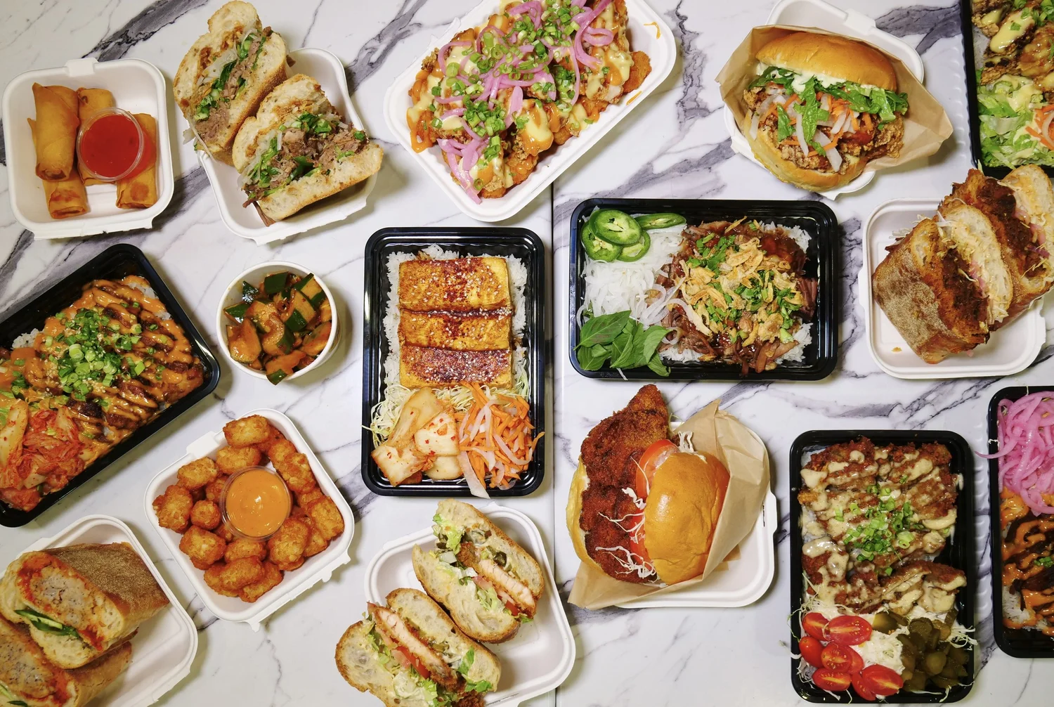 Sandwiches, rice bowls, tots and spring rolls laid out on a marble counter