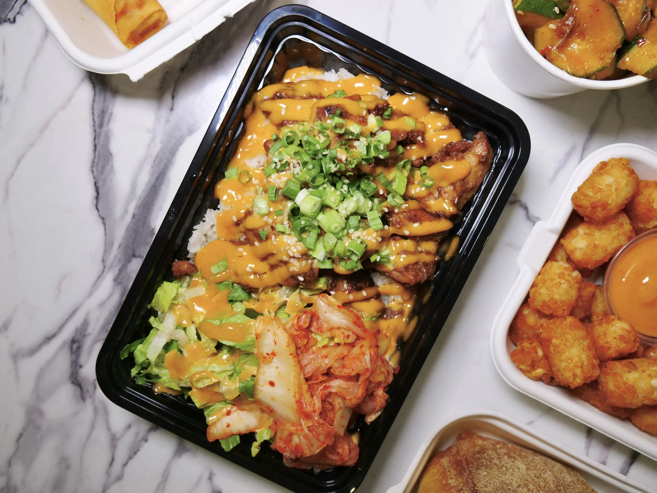 Korean BBQ rice bowl with gochujang, scallions, kimchi and lettuce in a black takeout tray