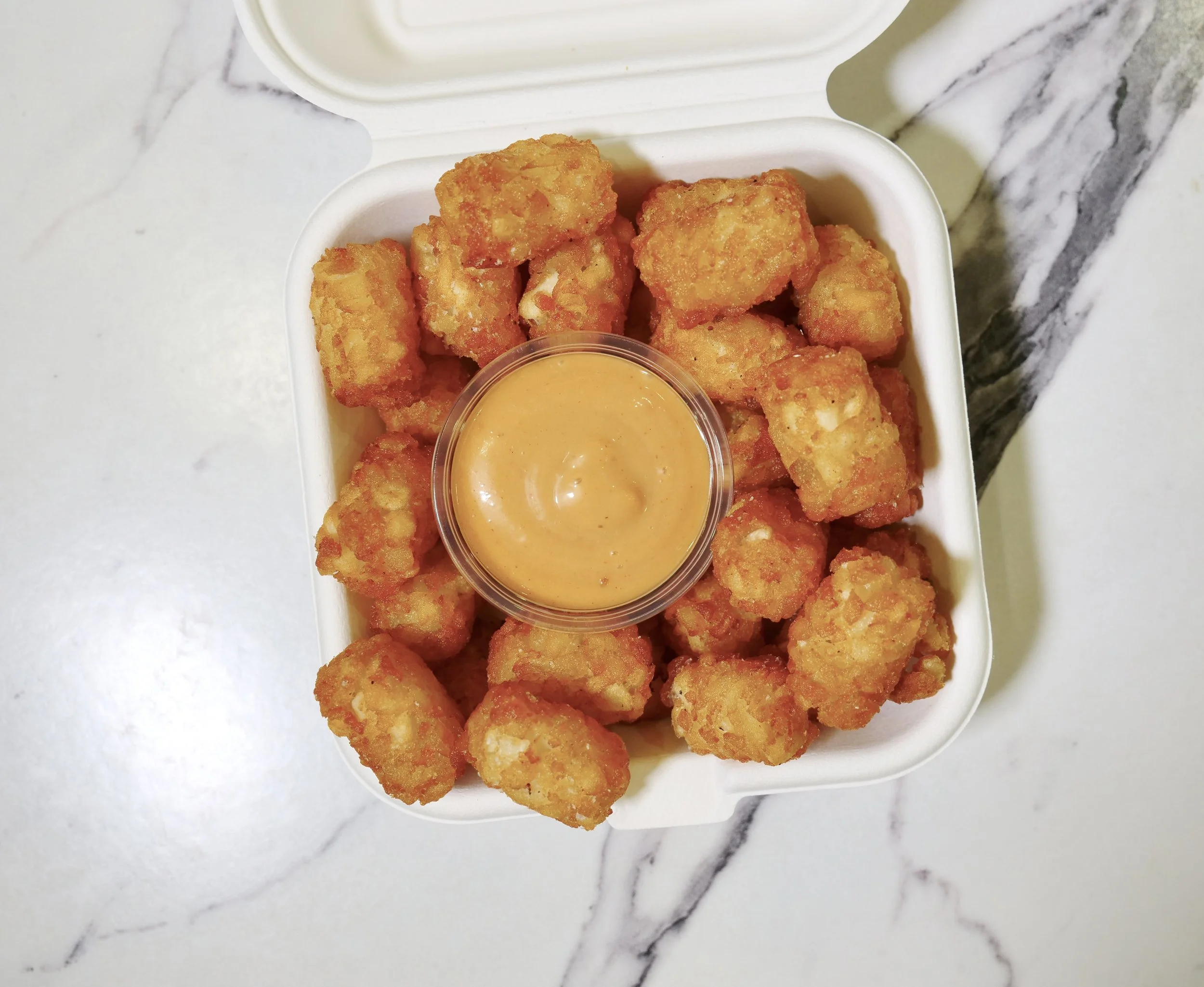Crispy Kirin Tots with dipping sauce in a takeout clamshell