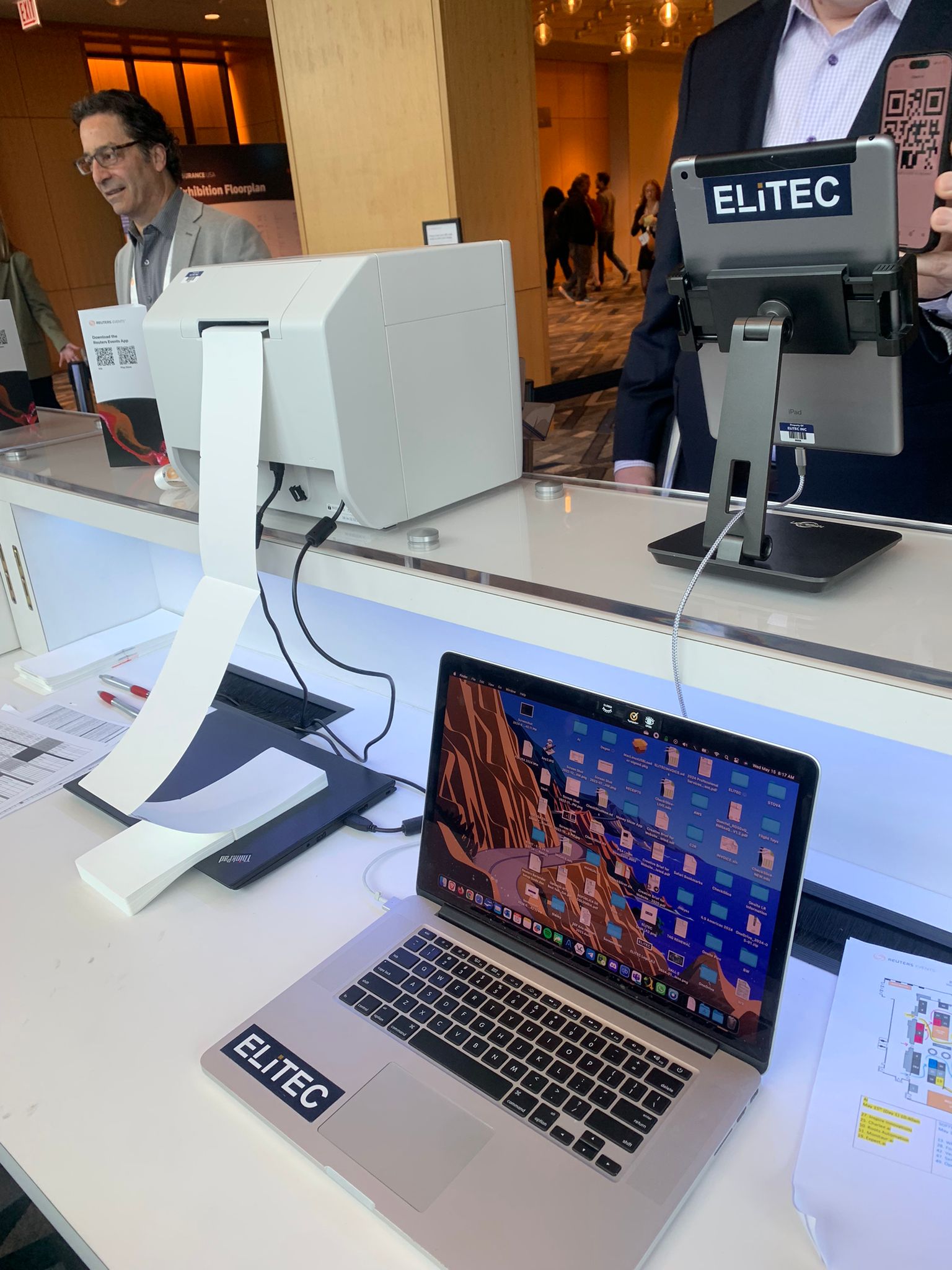 ELiTEC-branded MacBook and iPad registration hardware on a conference check-in desk