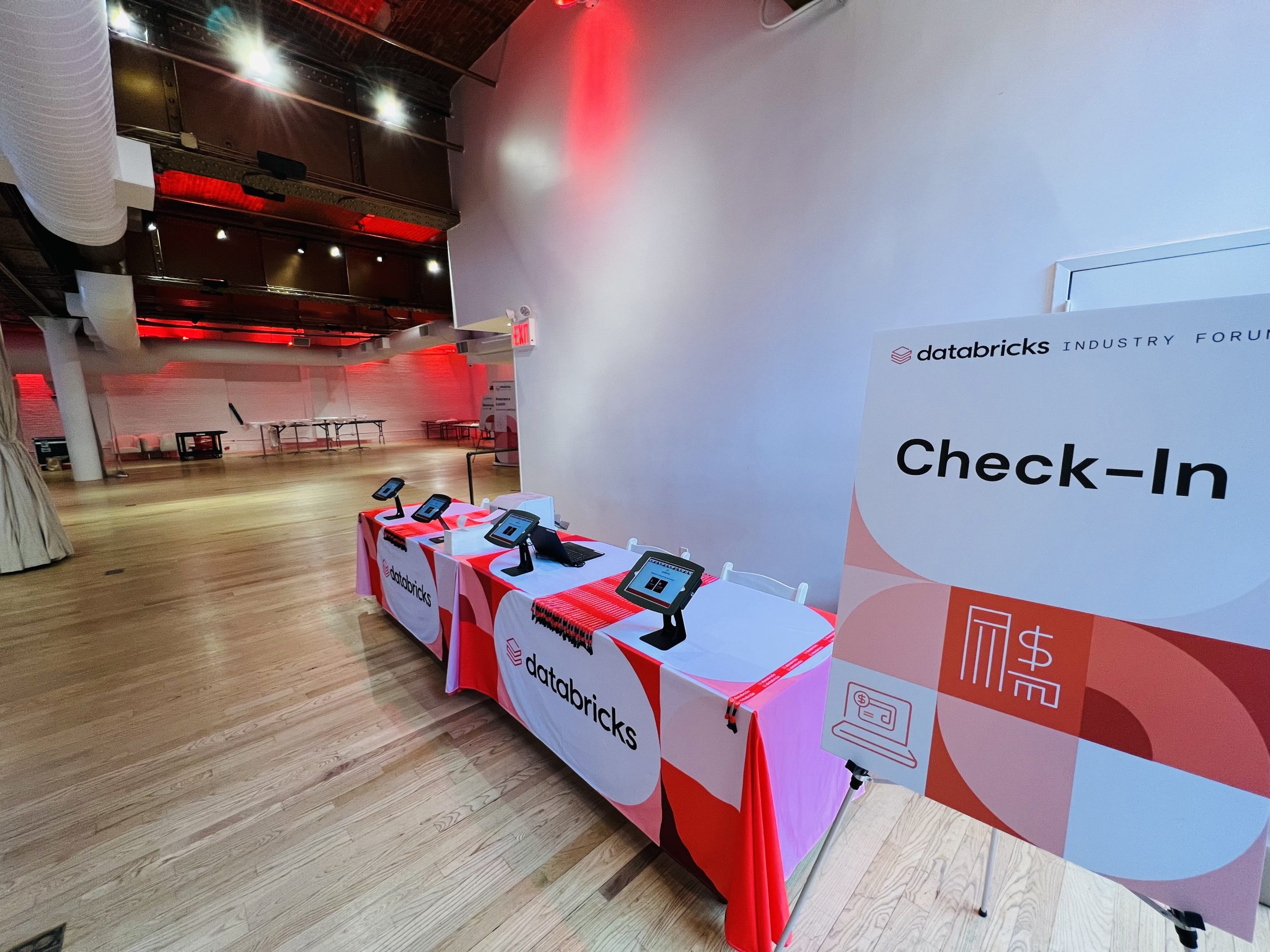 Databricks Industry Forum check-in table with iPad kiosks under red venue lighting