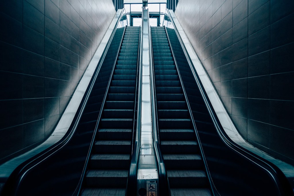 Looking up at two empty escalators rising toward a bright window