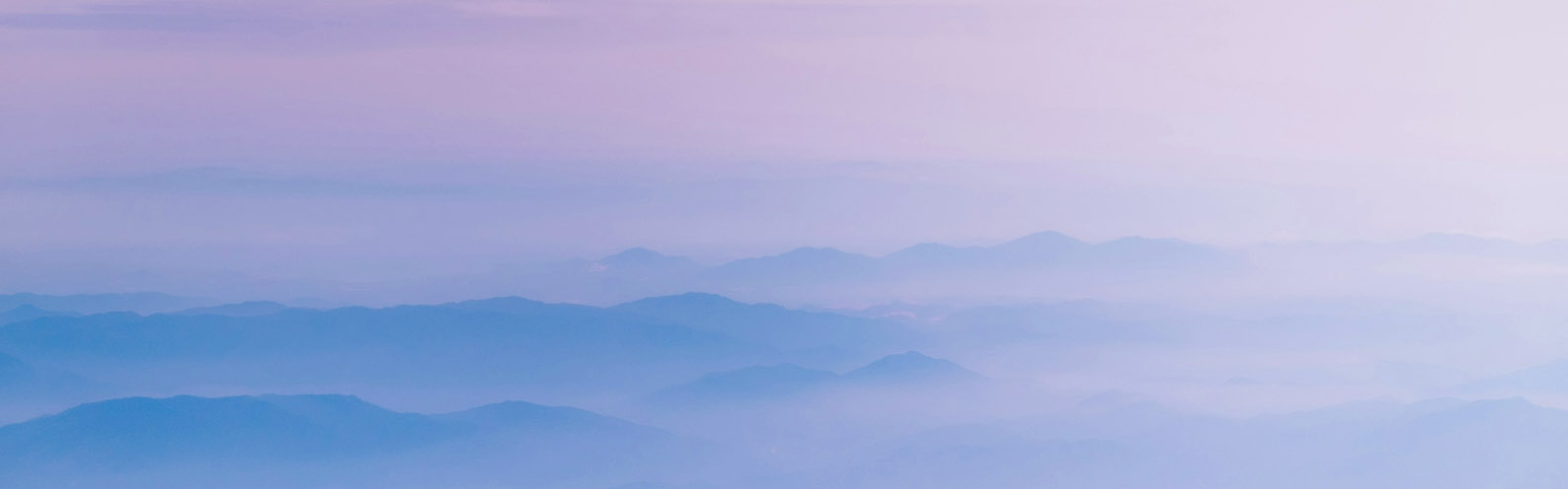 Layered mountain ridges wrapped in soft blue-lavender mist at dawn