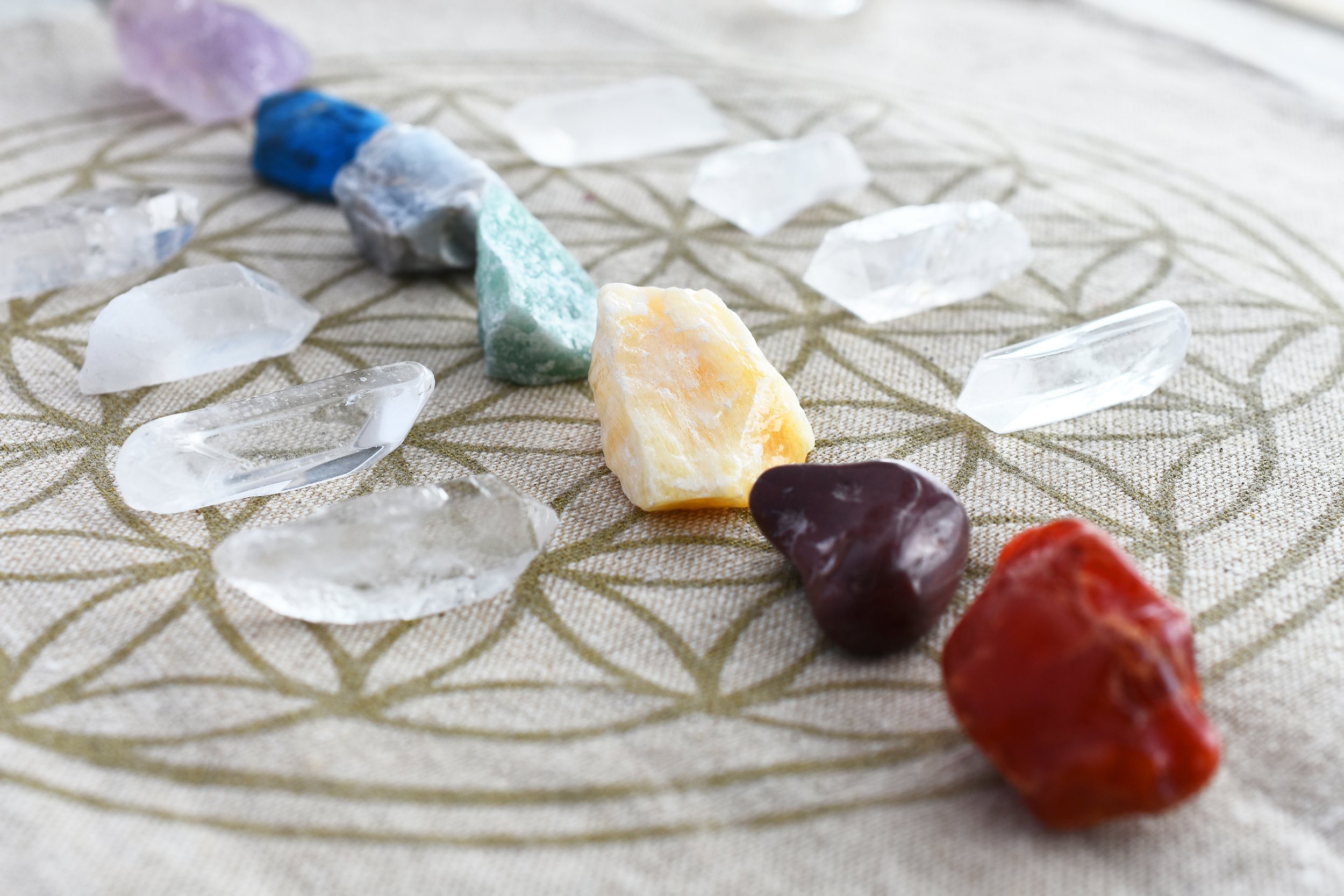 Chakra crystals and gemstones arranged on a flower-of-life patterned fabric