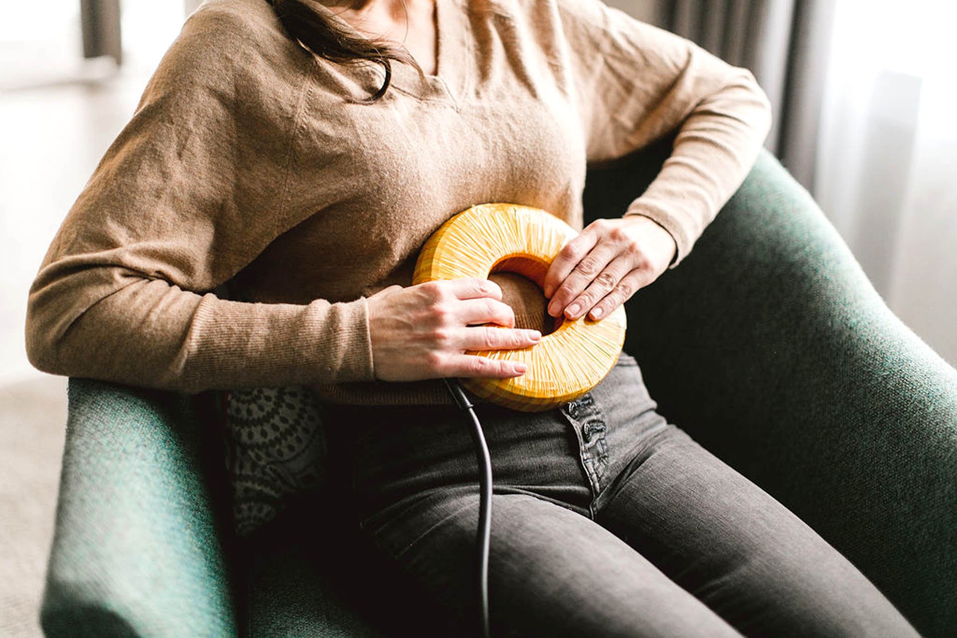 A woman holding a torus-shaped PEMF AmpCoil device against her abdomen while seated