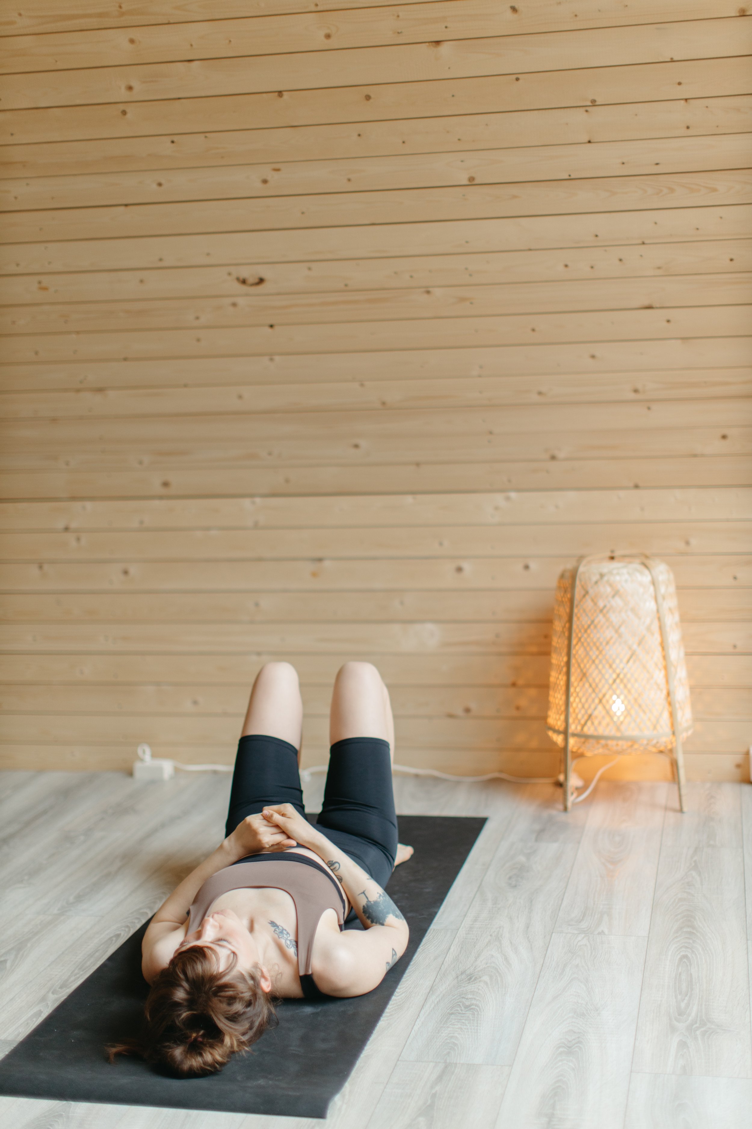 A woman lying on a yoga mat on a wooden floor with her hands resting on her chest