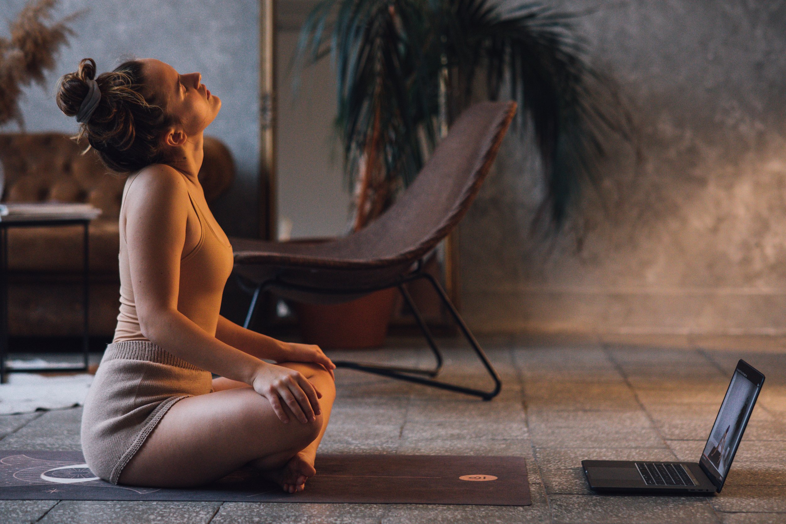 A woman on a yoga mat with a laptop open beside her for a remote session
