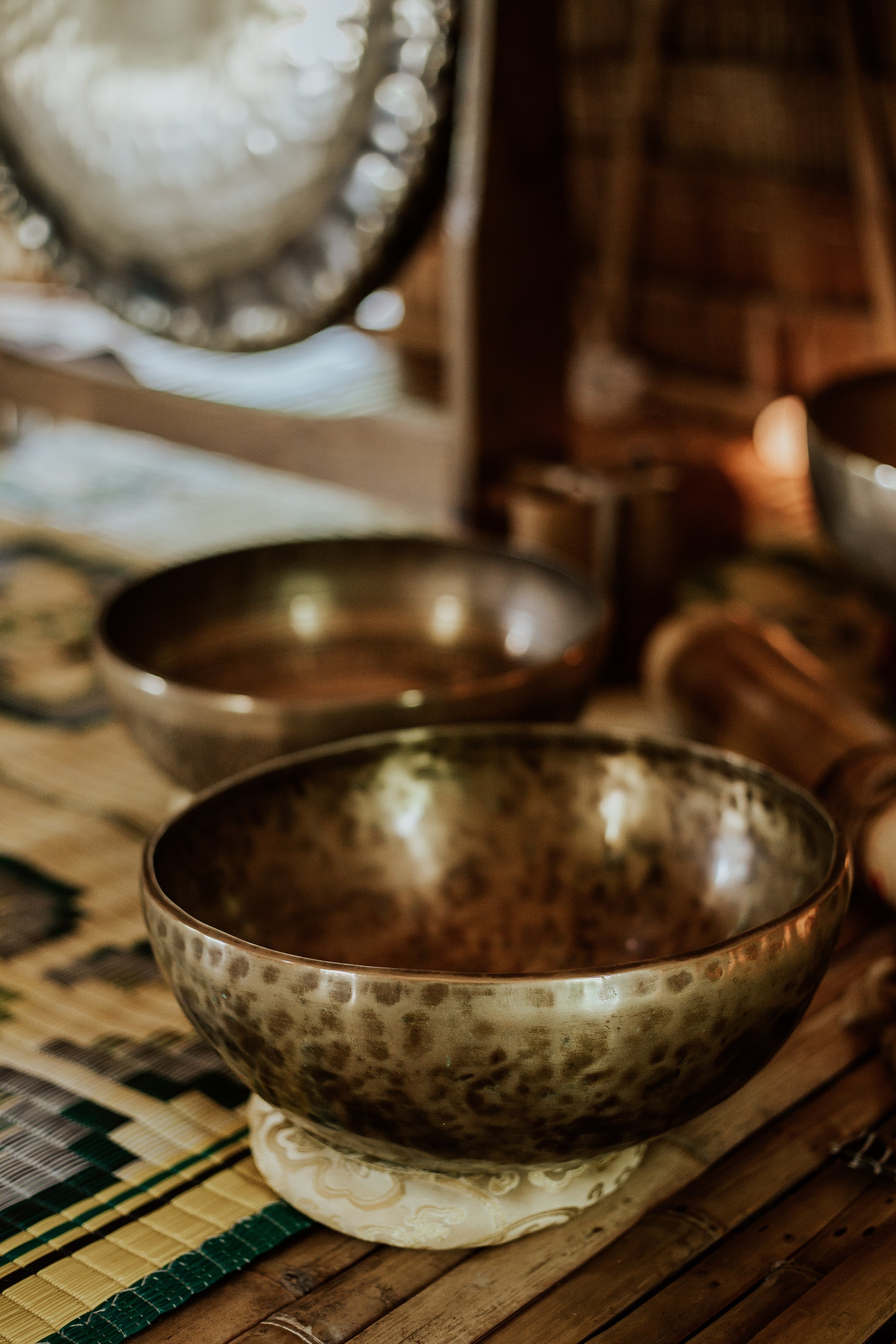 Tibetan singing bowls arranged on a bamboo mat with a candle nearby