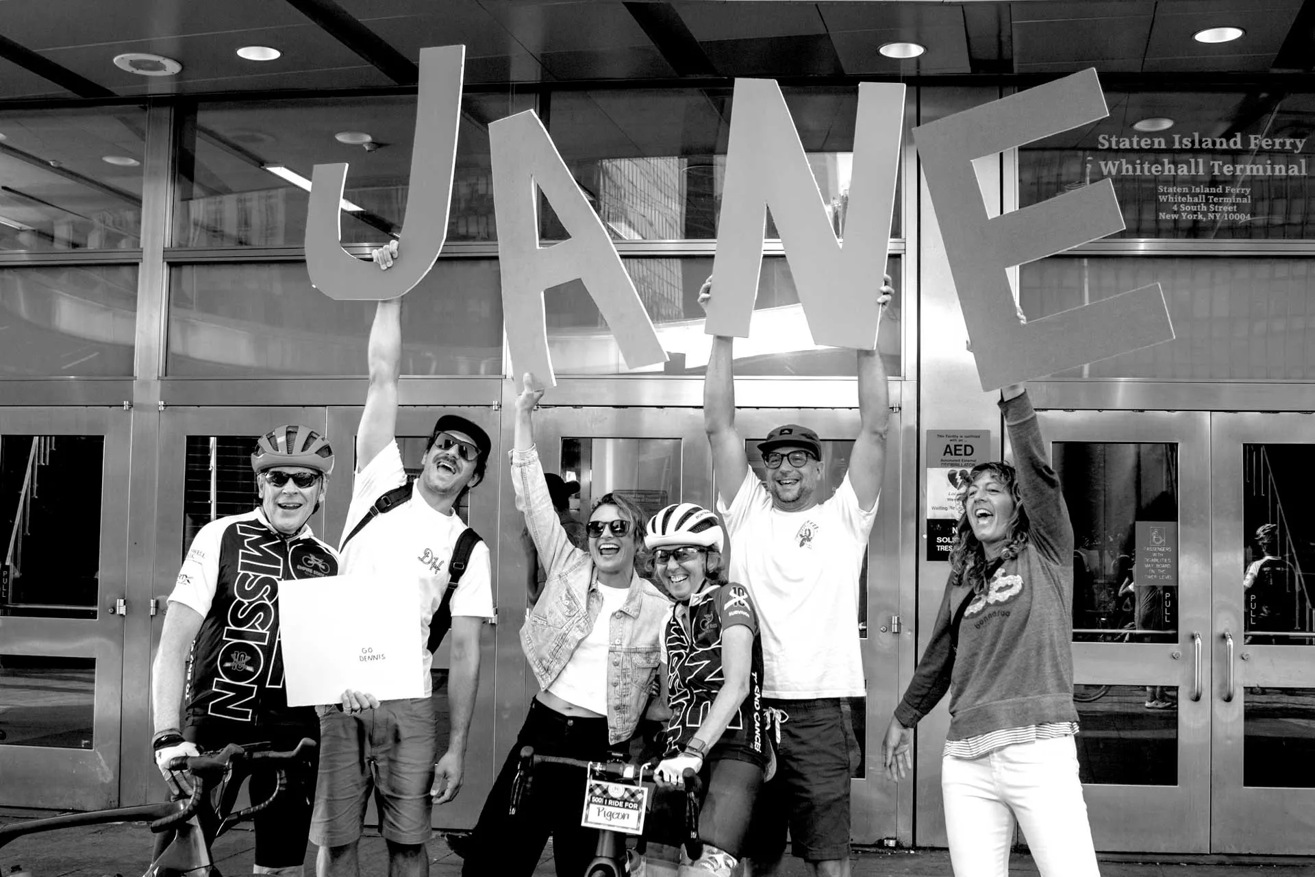 Riders outside the Staten Island Ferry terminal holding letters spelling JANE