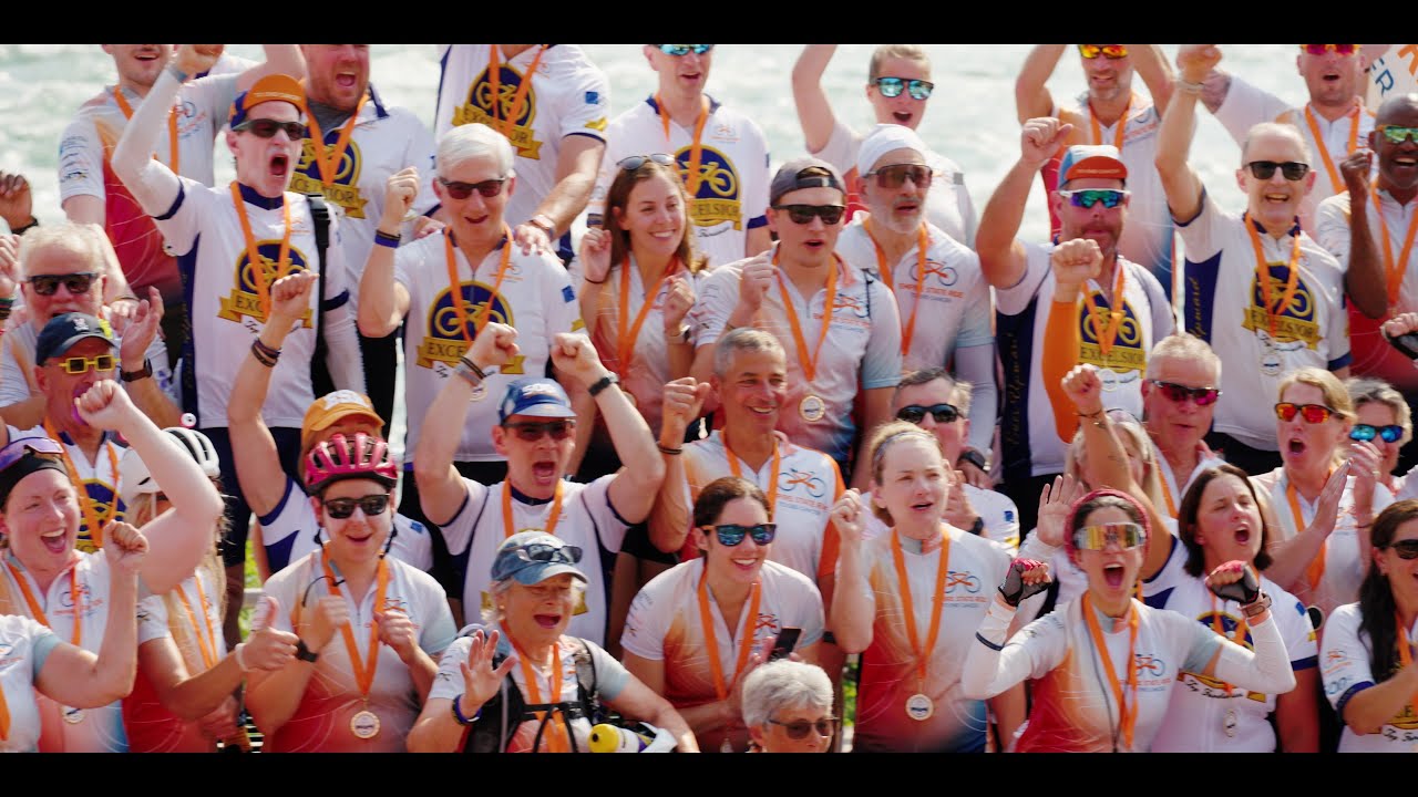 Jubilant Empire State Ride cyclists in white and orange jerseys celebrating with medals at the finish