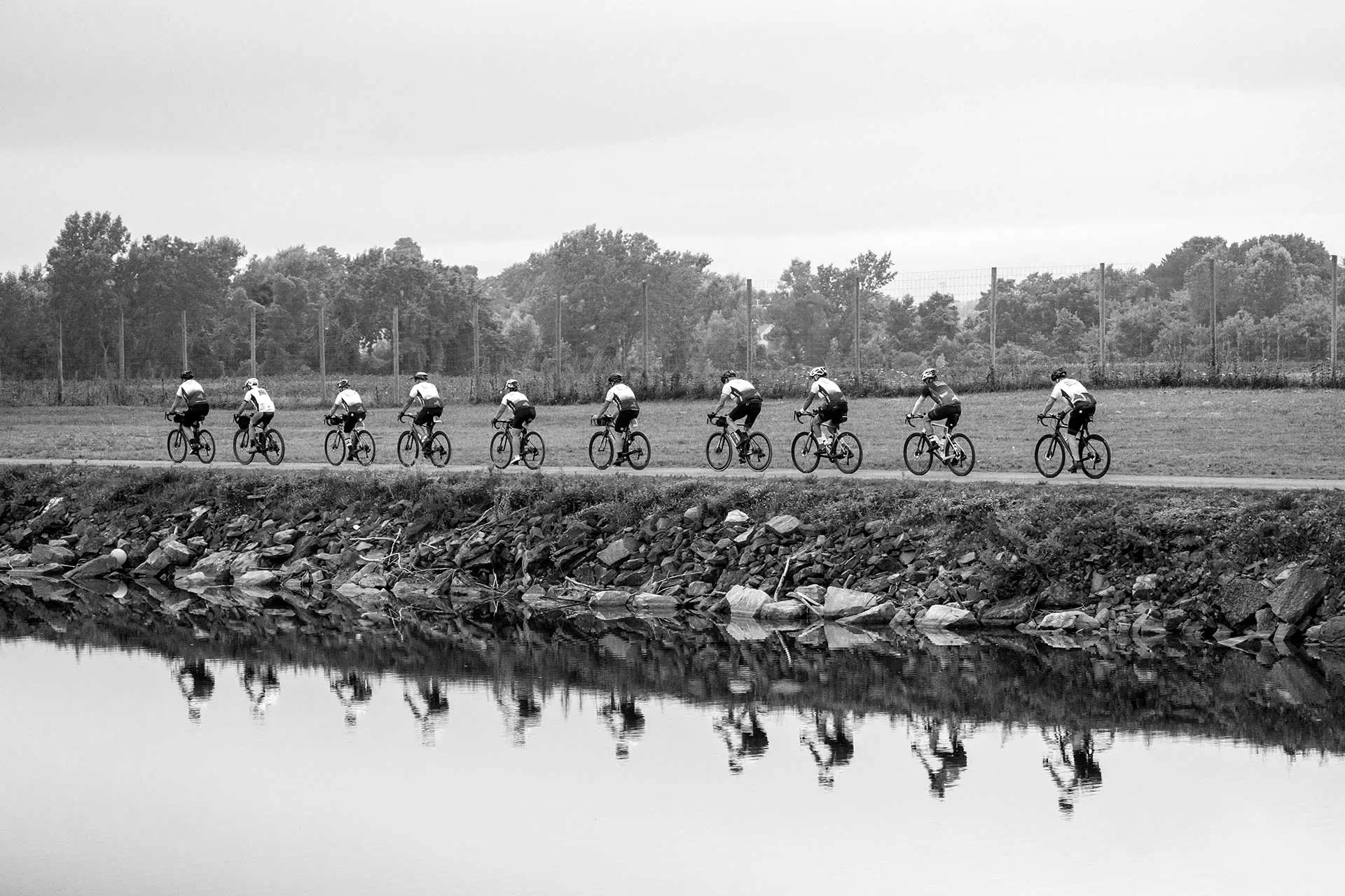 Line of cyclists riding a rural road beside a canal