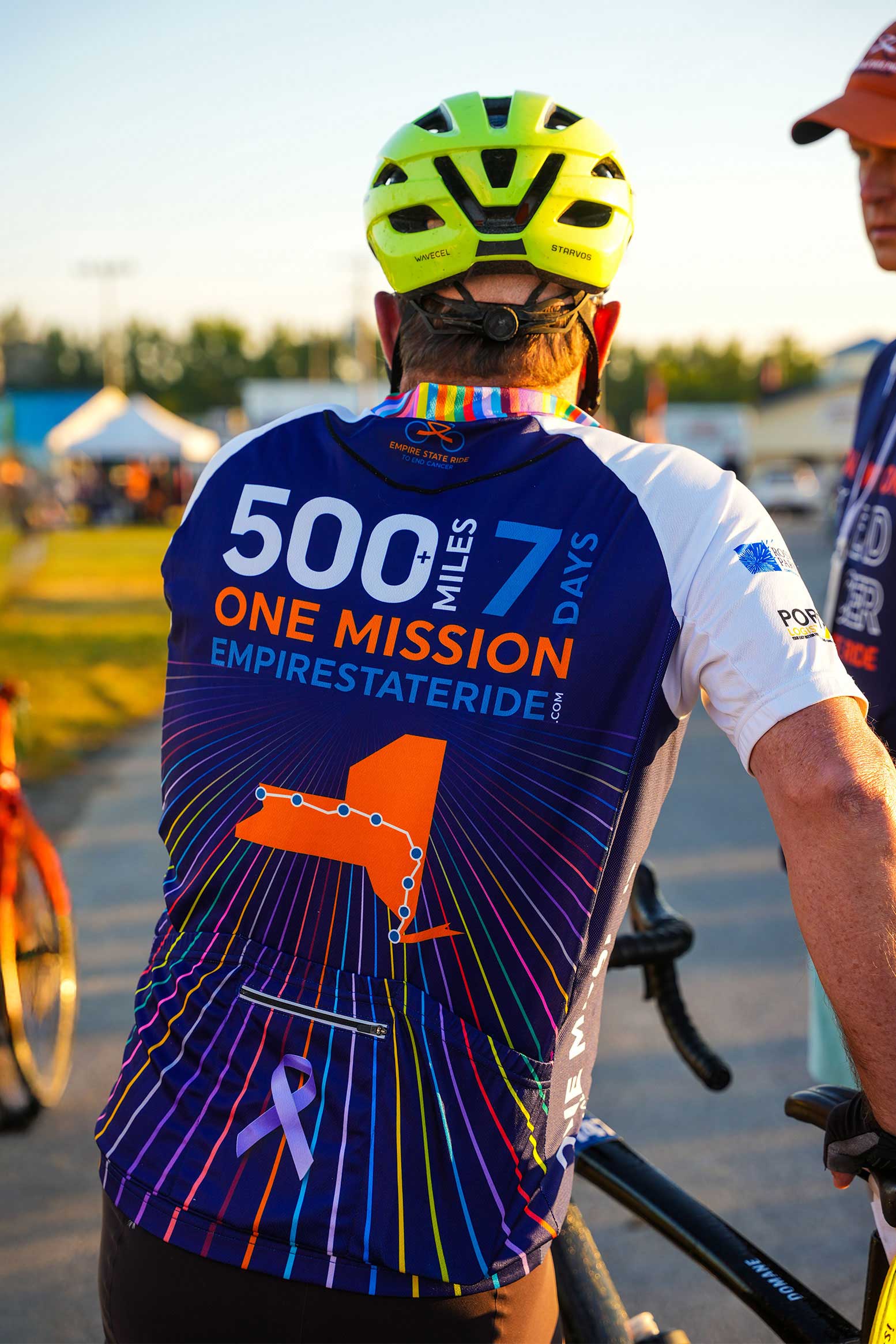 Cyclist from behind wearing an Empire State Ride jersey reading 500+ Miles, 7 Days, One Mission