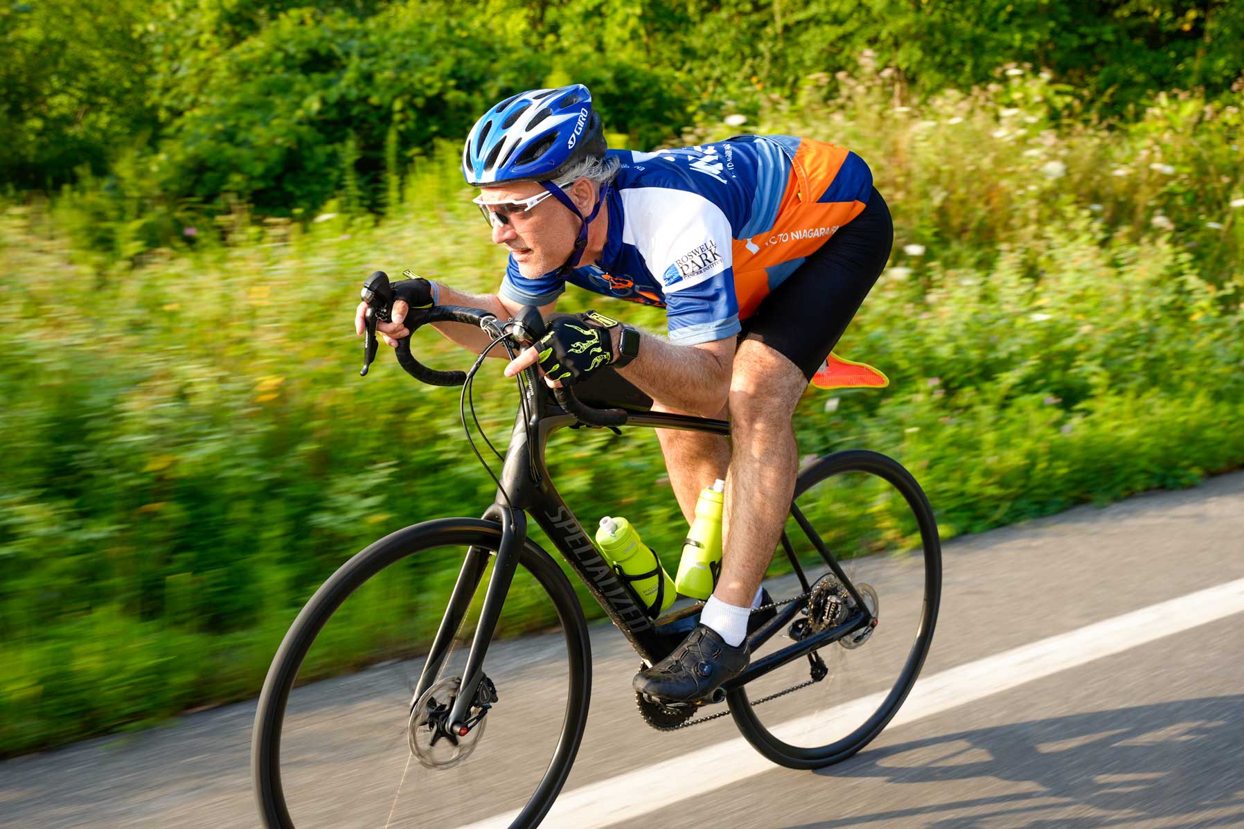 Older male rider in a blue and orange Empire State Ride jersey riding at speed
