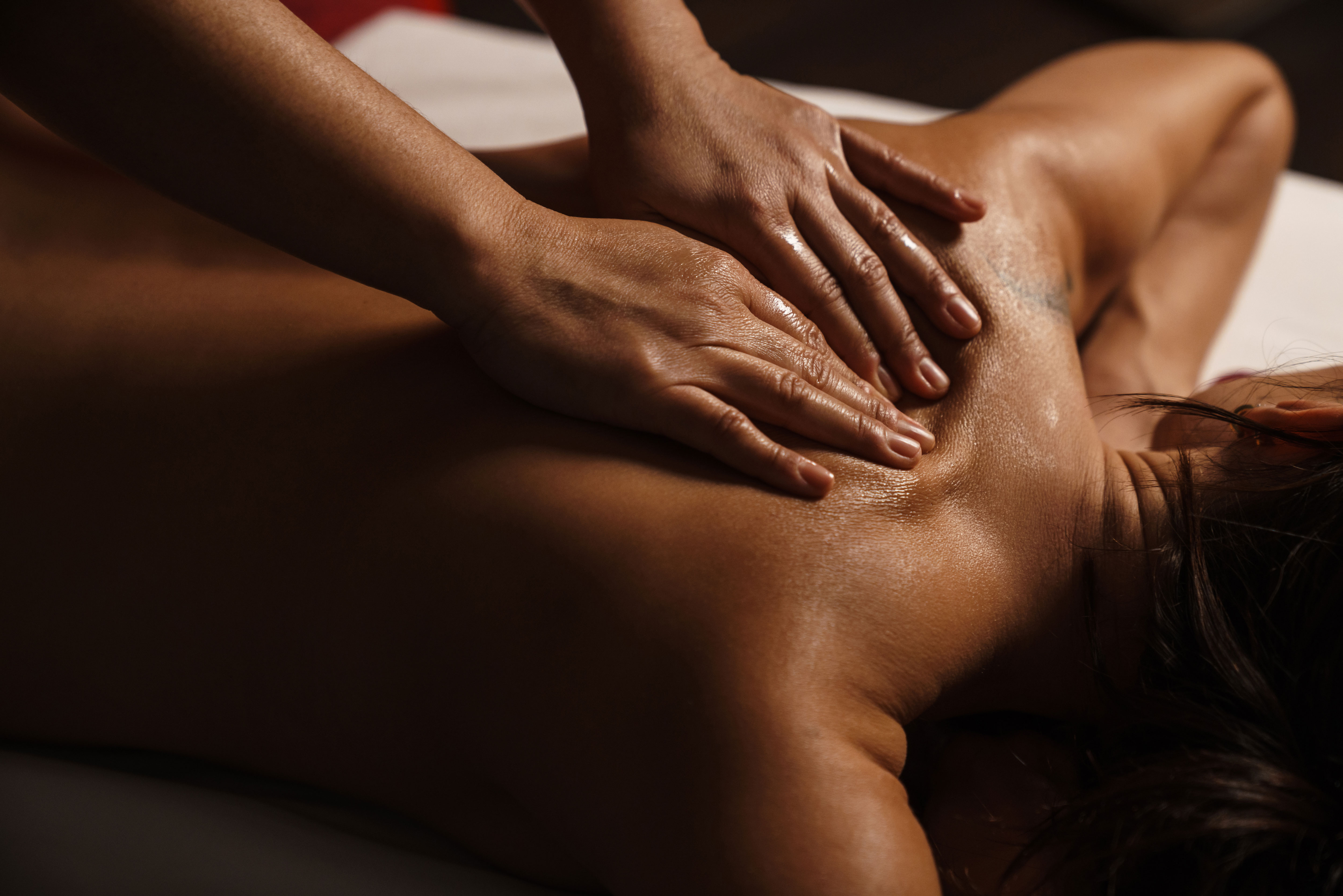 Therapist's hands performing a back massage on a client lying face down in warm light