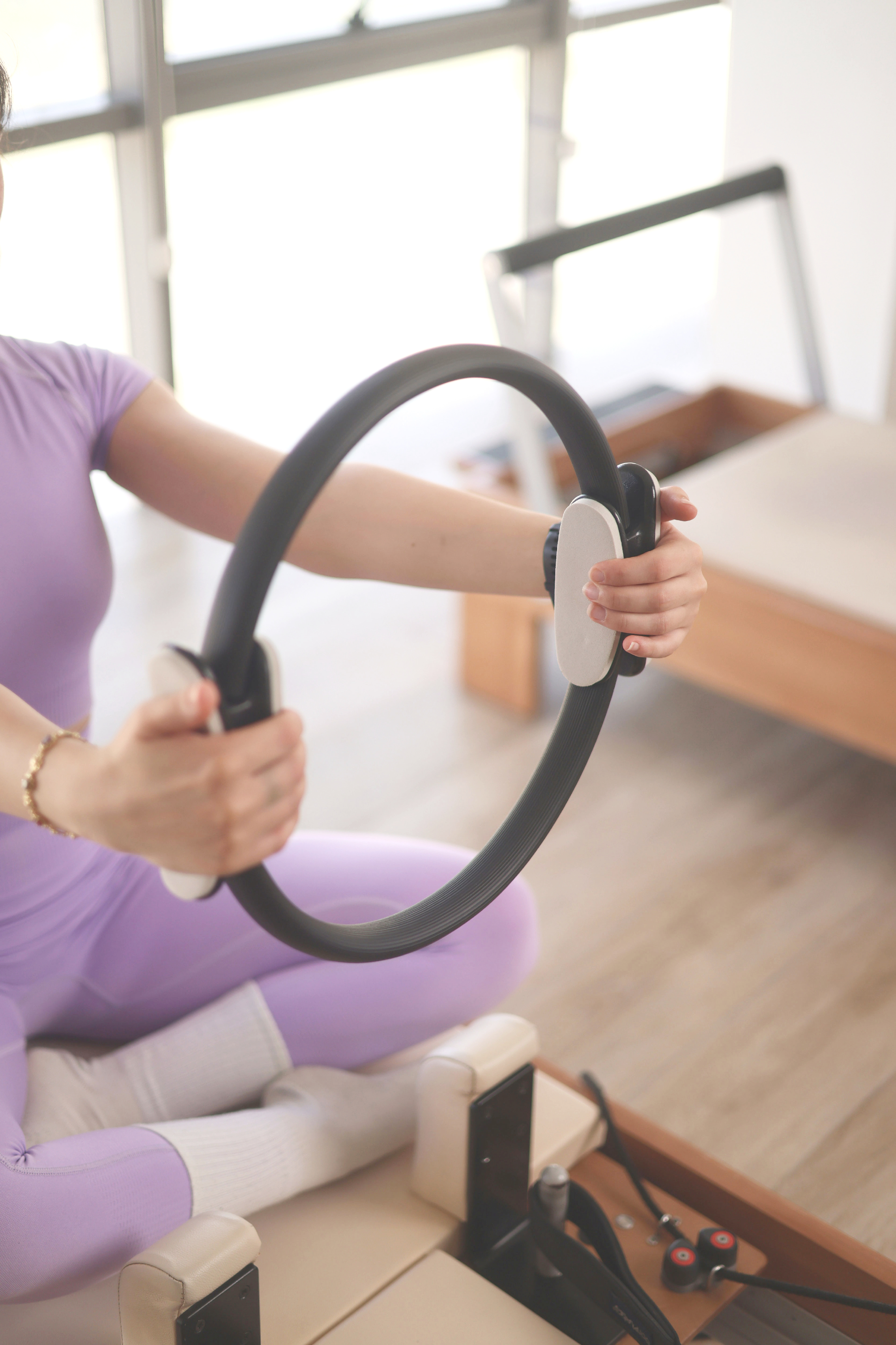 Client holding a Pilates ring on a reformer machine in a bright studio