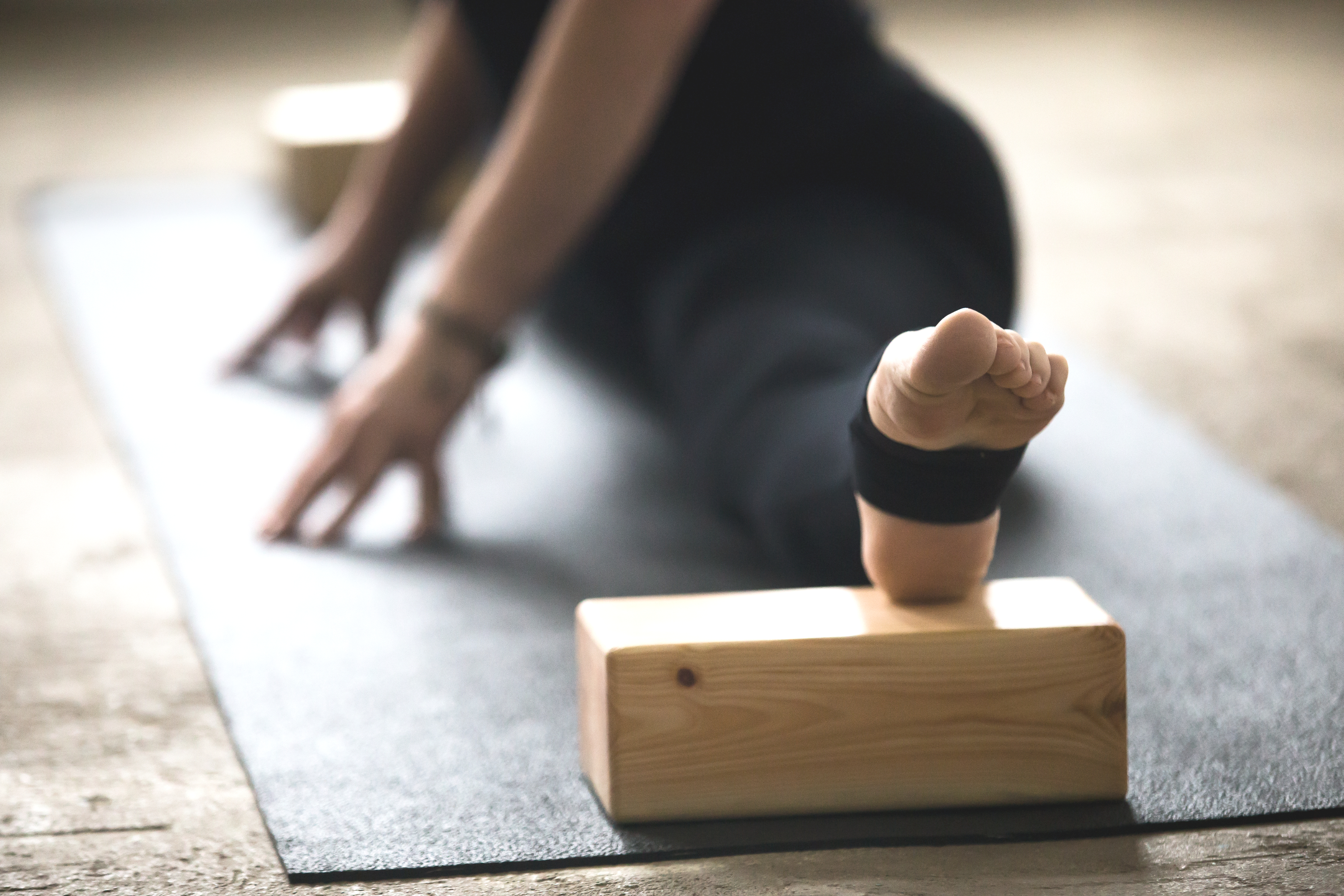Person in black activewear in a yoga forward fold with a wooden block