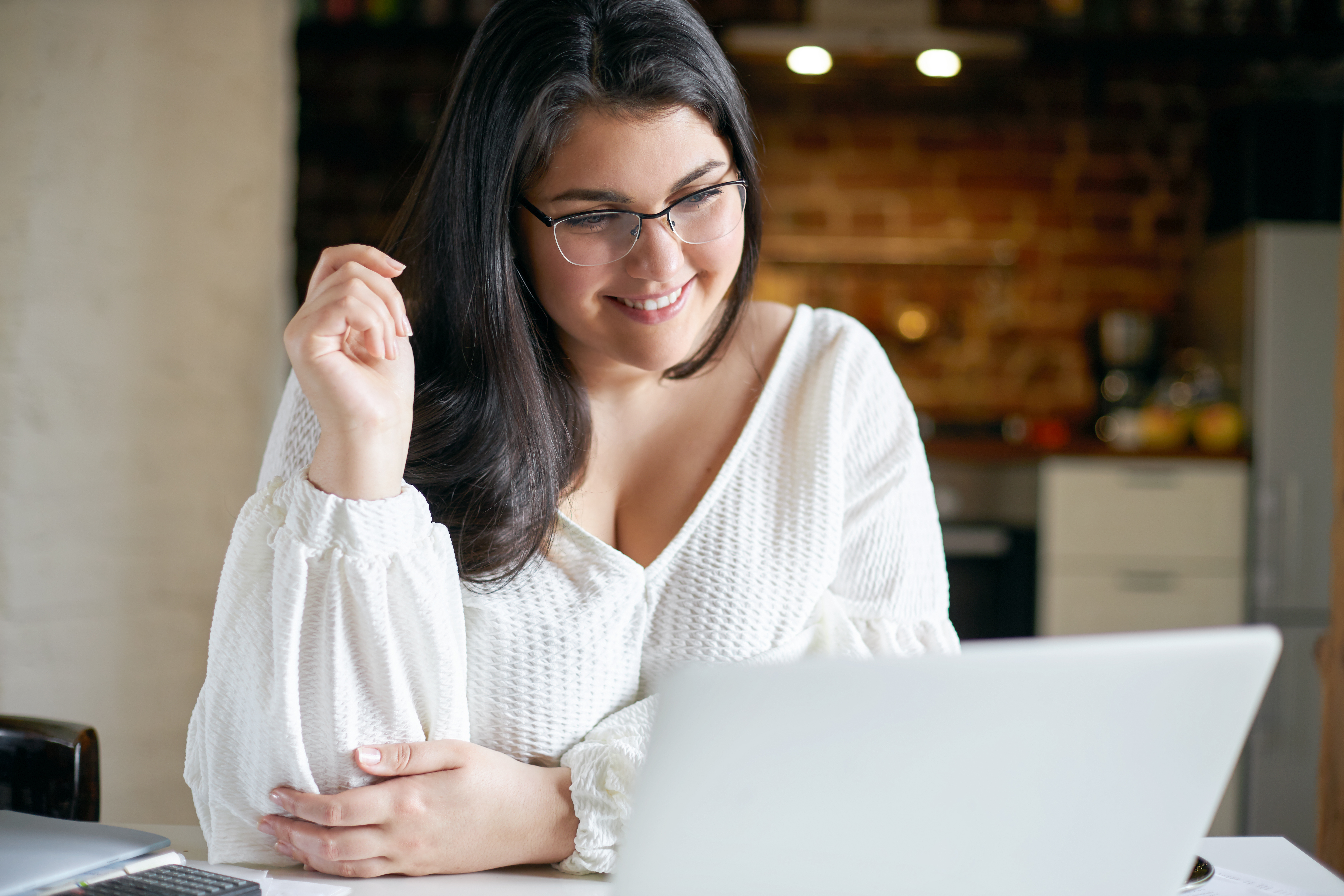 A woman with glasses smiling at her laptop during a coaching session