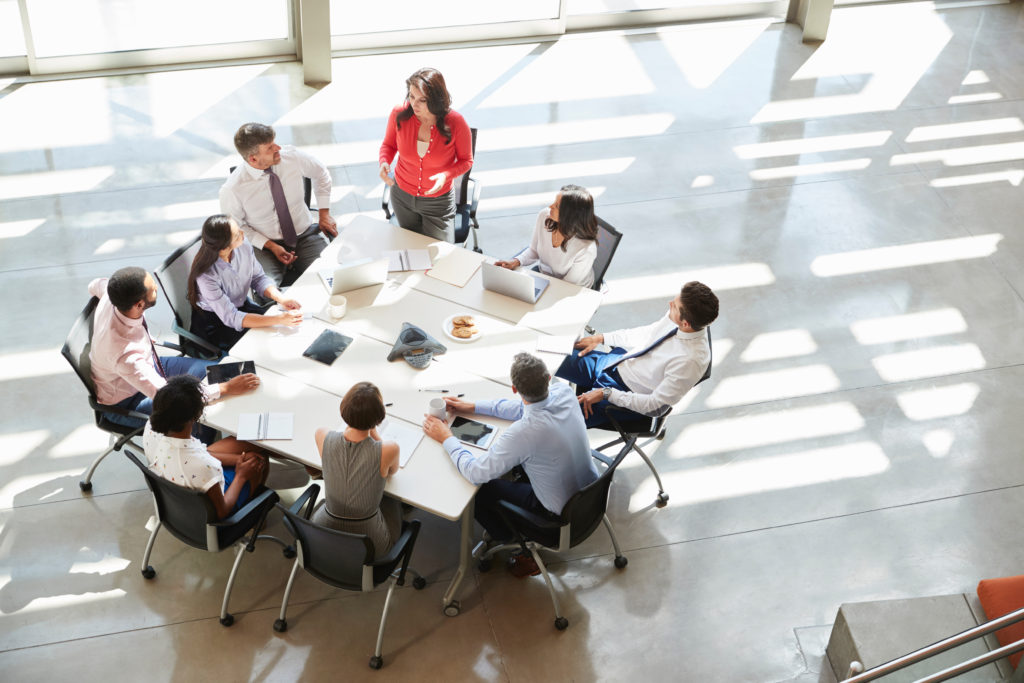 Business team around a round conference table with a woman in red presenting