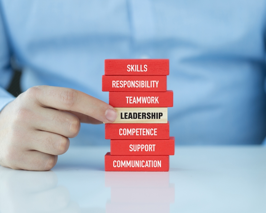 Hand stacking red blocks labeled with leadership concepts