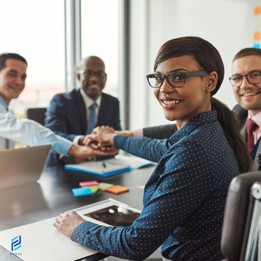 Four business professionals smiling and joining hands at a conference table