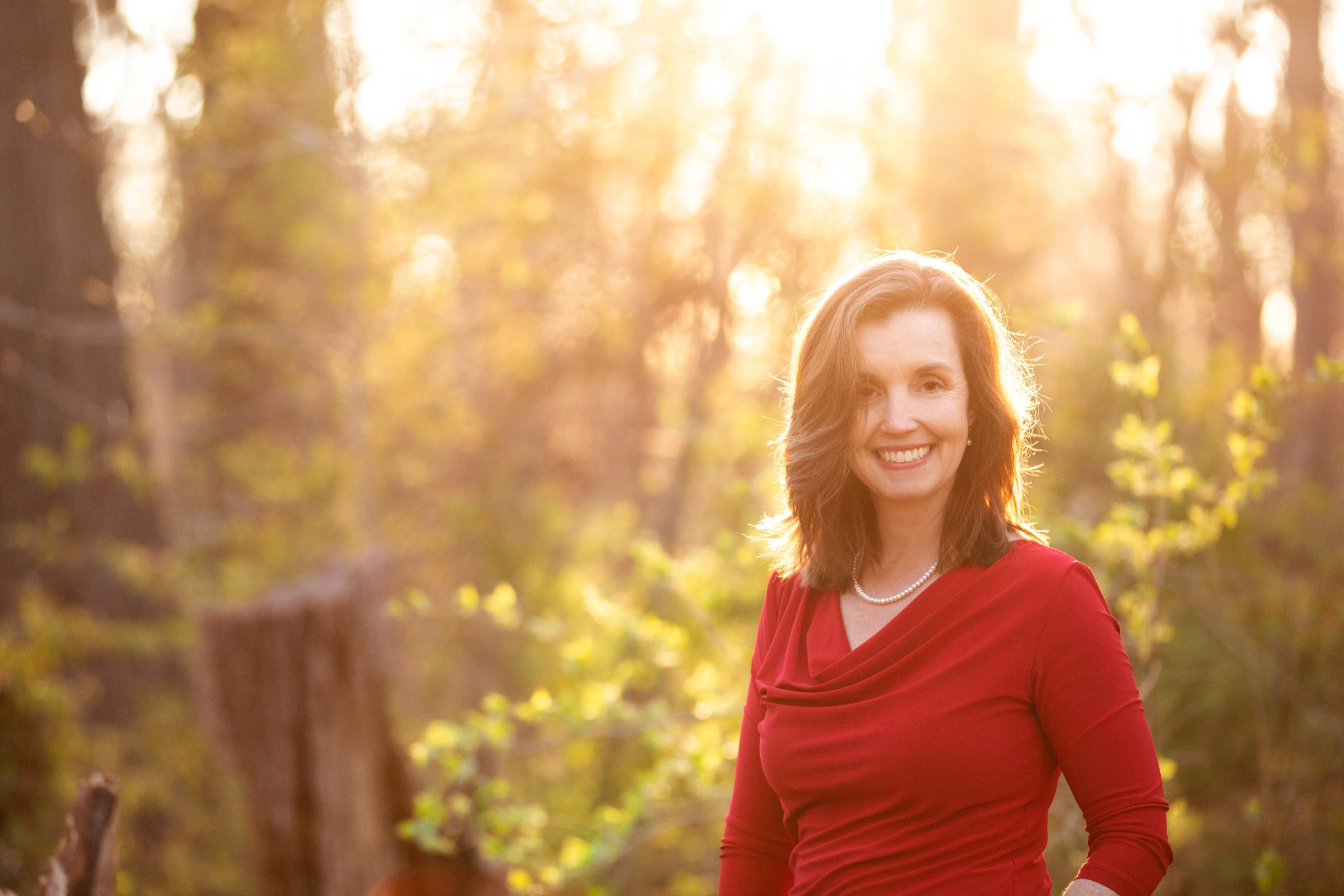 Erin Owen smiling in a sunlit forest, wearing a red top