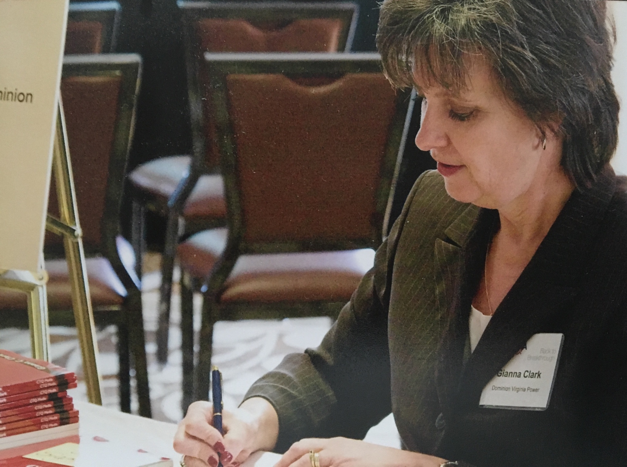 Gianna Clark signing books at a conference table with stacks of red books